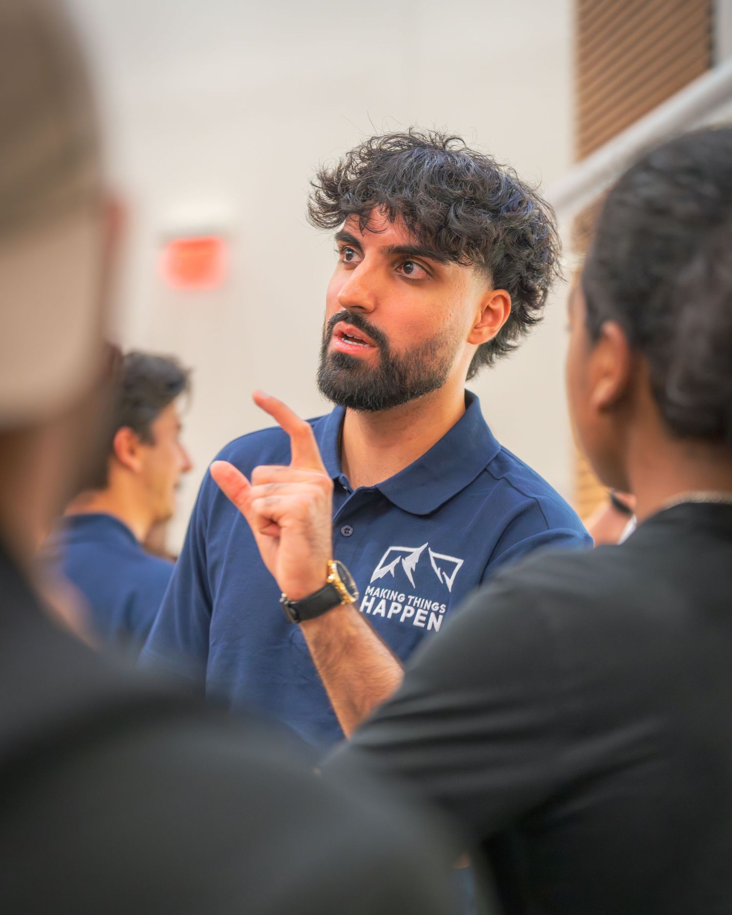 Speaker wearing navy branded shirt gesturing during animated discussion.