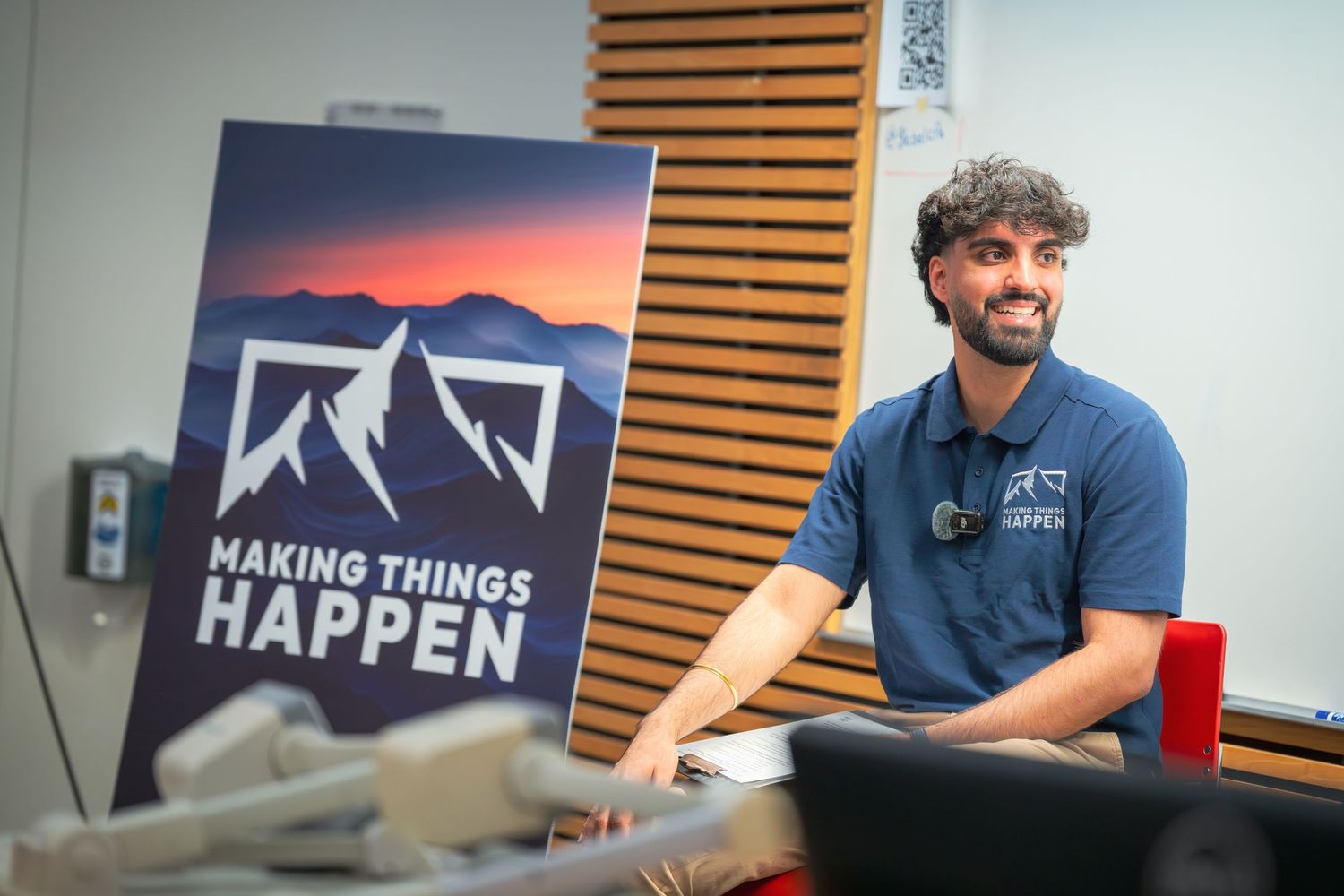 Presenter smiling in front of a Making Things Happen banner in a classroom setting.