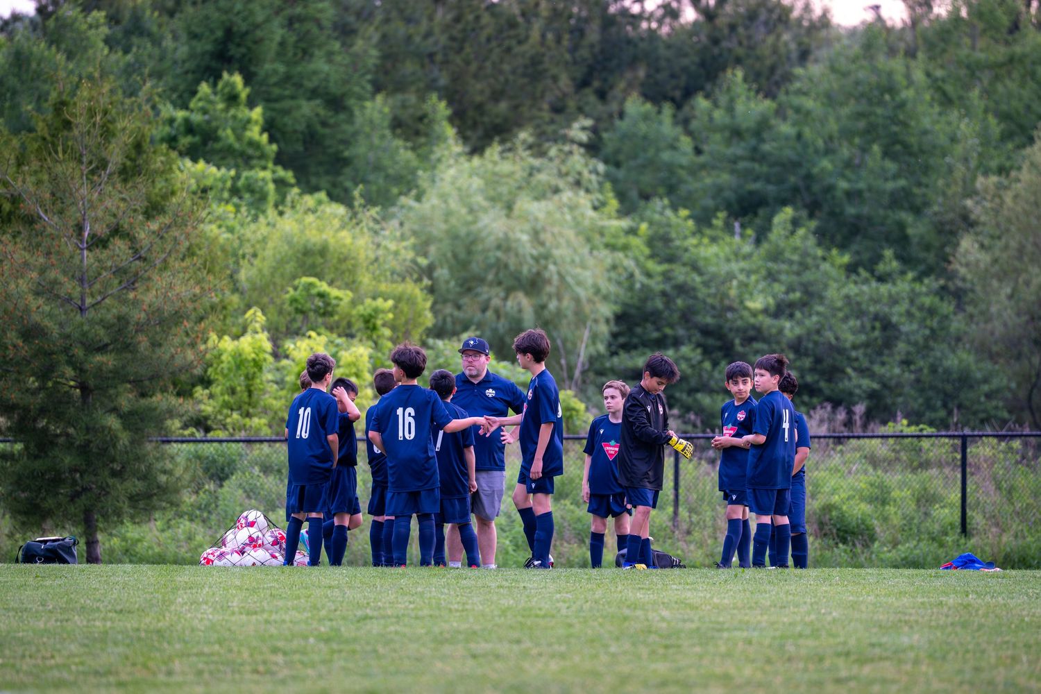 Soccer players gather together on a grassy field during a team meeting at sunset.