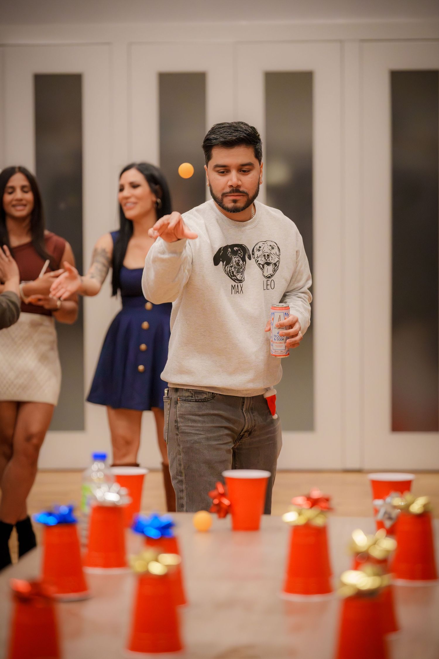 A person playing beer pong with red cups at an indoor party while others watch in the background.