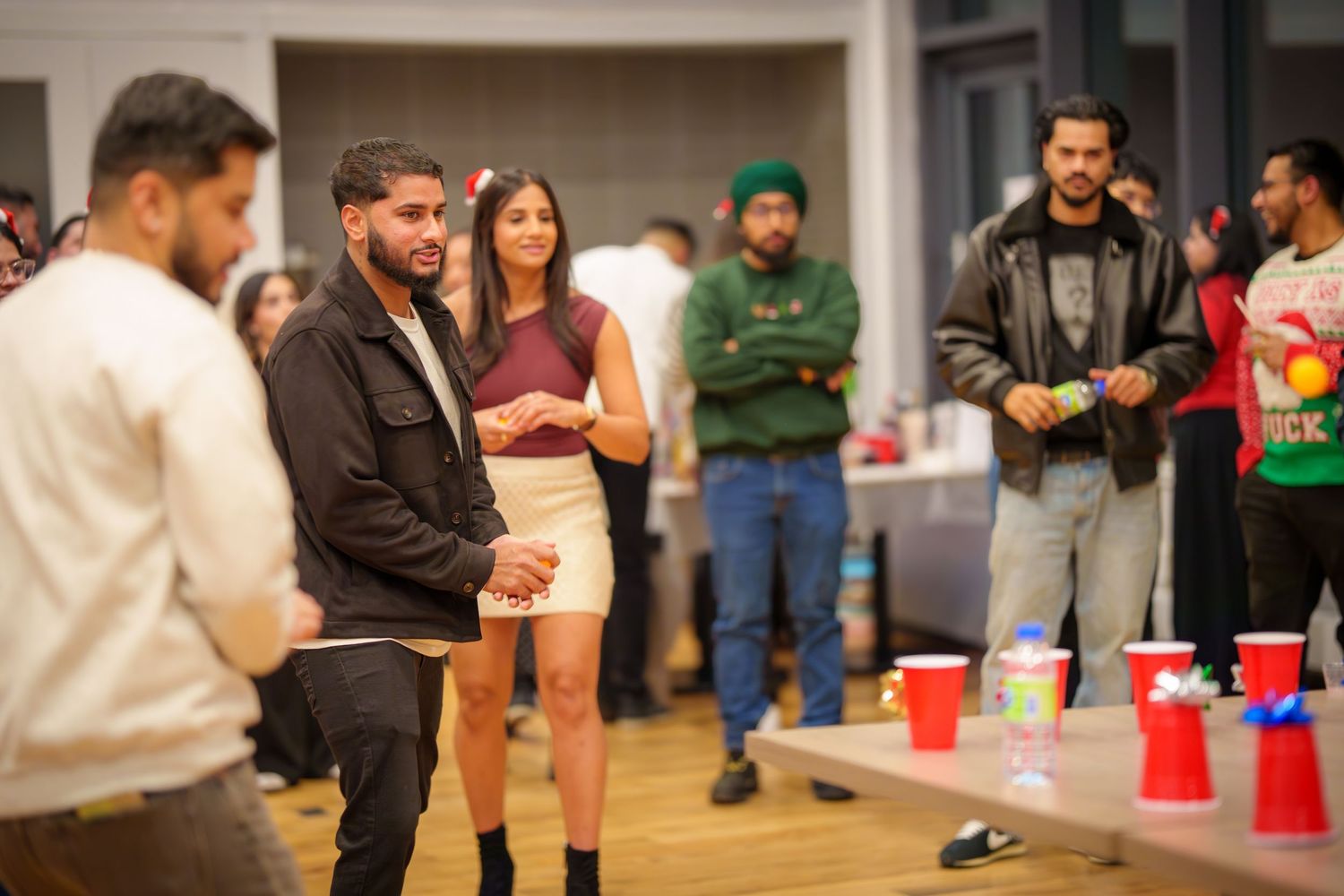 People gathered around red cups on a wooden floor during what appears to be a party game.