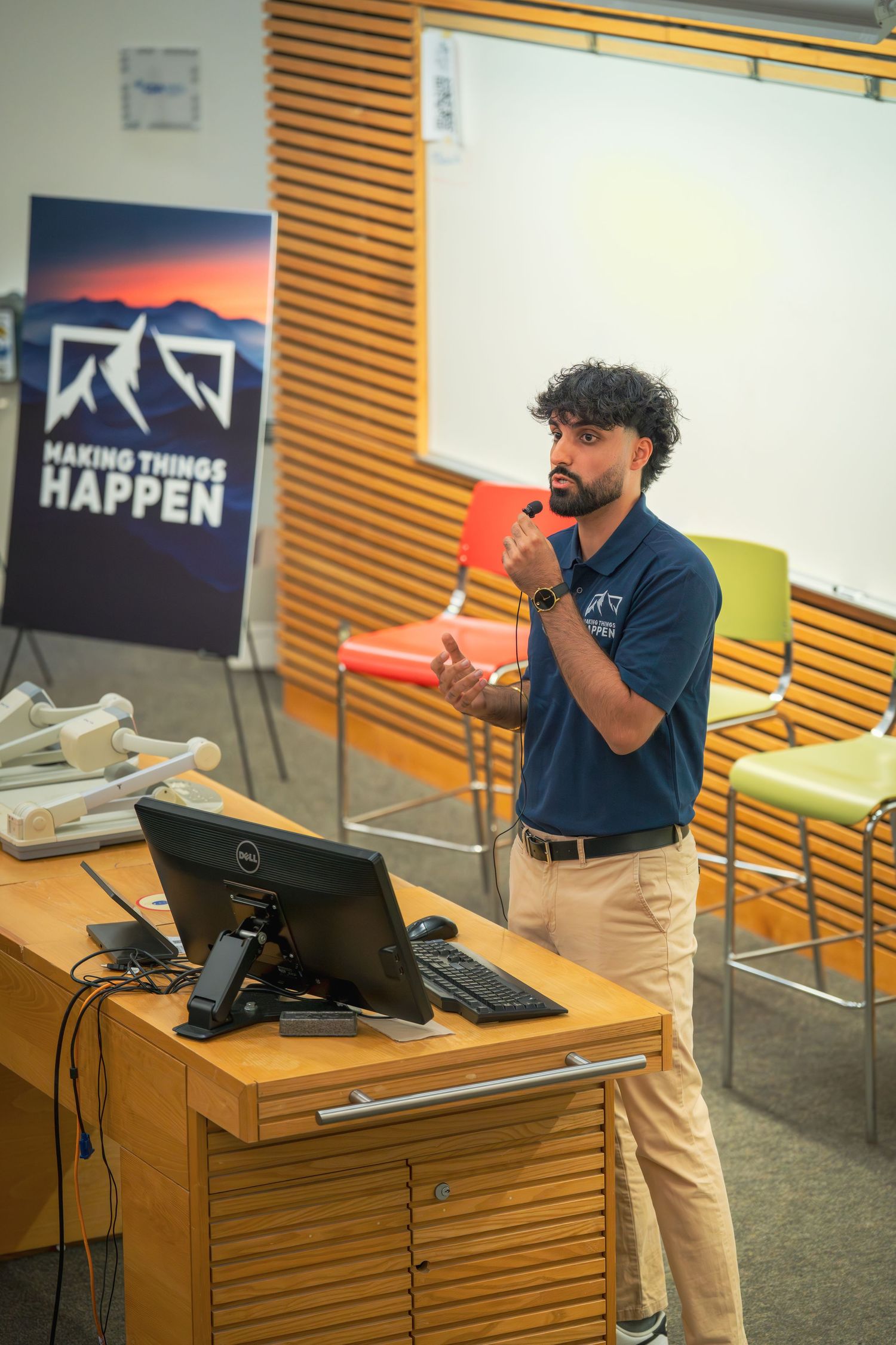 Presenter in navy polo and khakis speaks from wooden podium during business presentation.