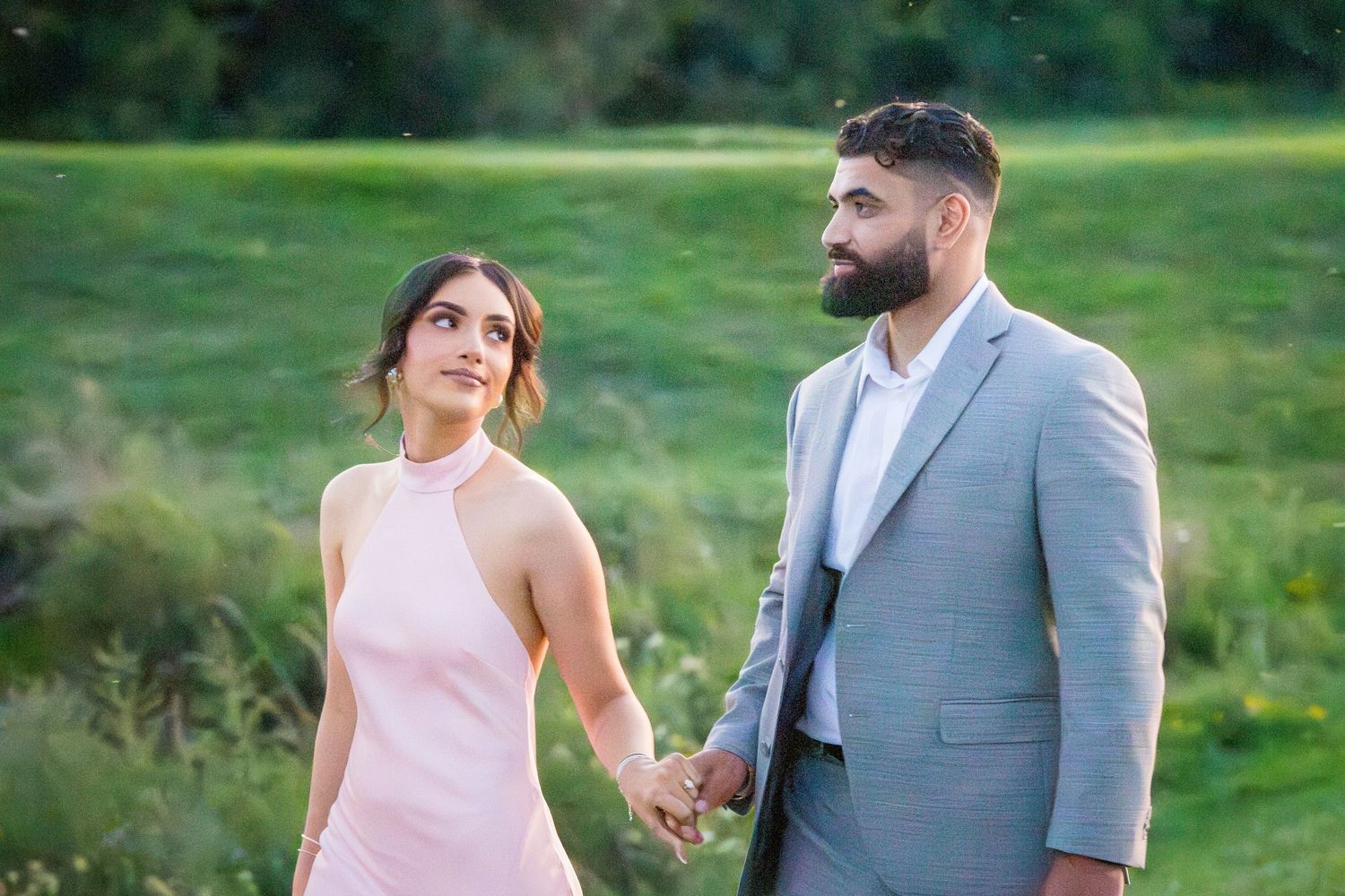 Two people in formal attire share a romantic moment on a path during golden hour.