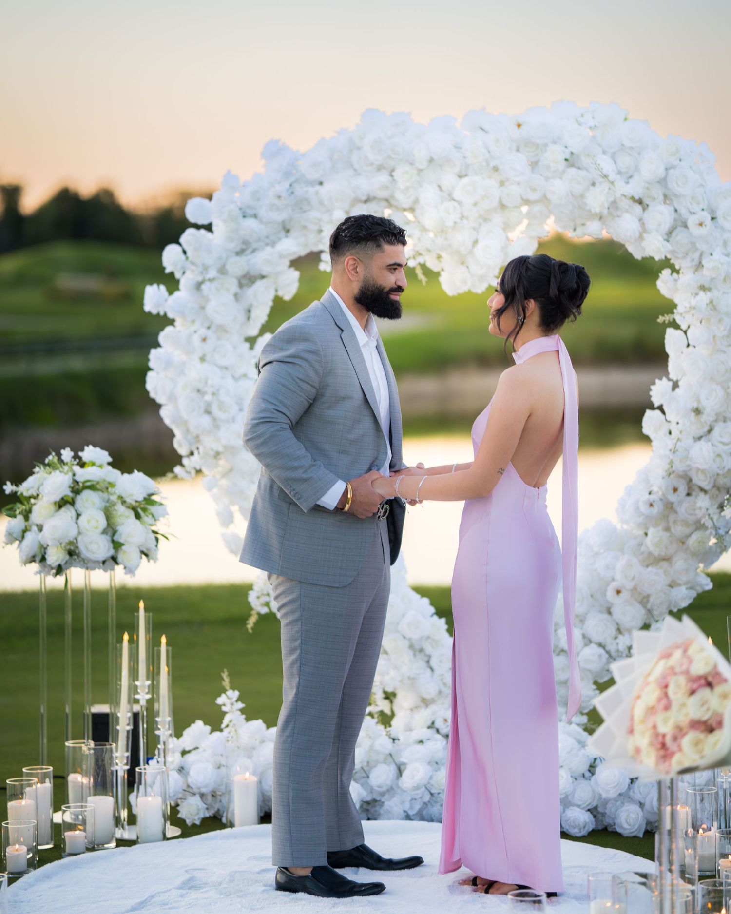 A couple shares a special moment under a white floral arch at sunset.