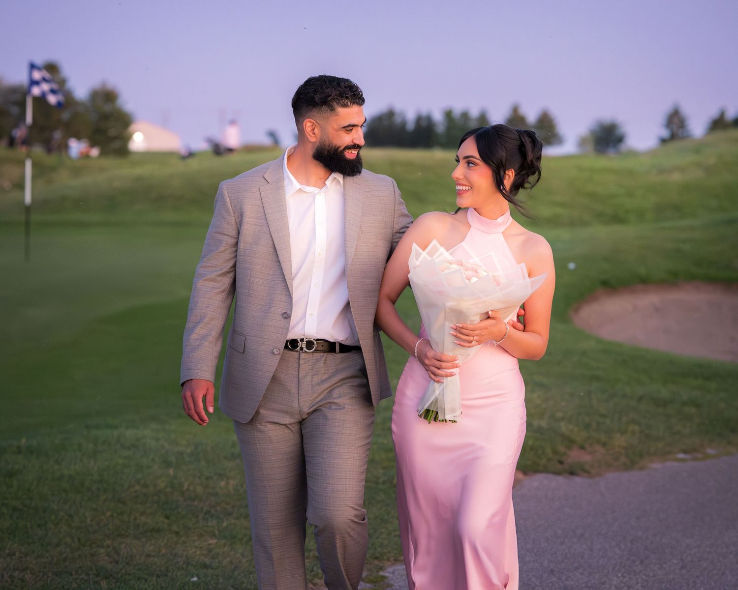 A couple shares an intimate moment while walking on a gravel path at sunset.