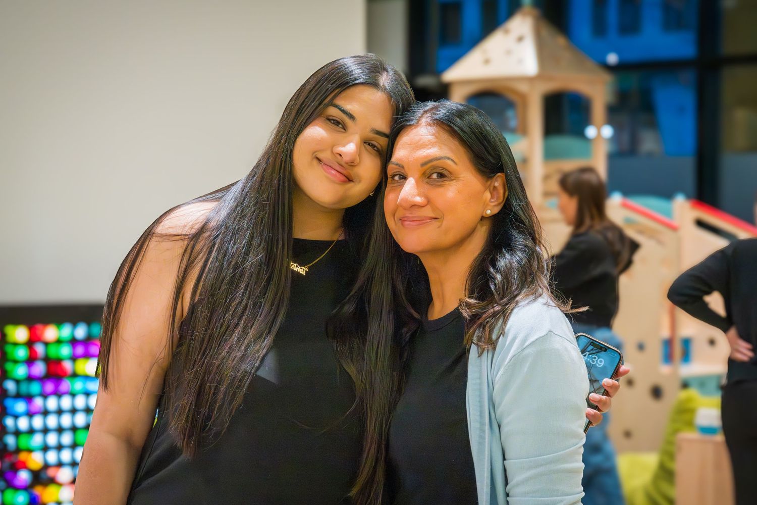 Two young women with long dark hair smiling together at an indoor event.