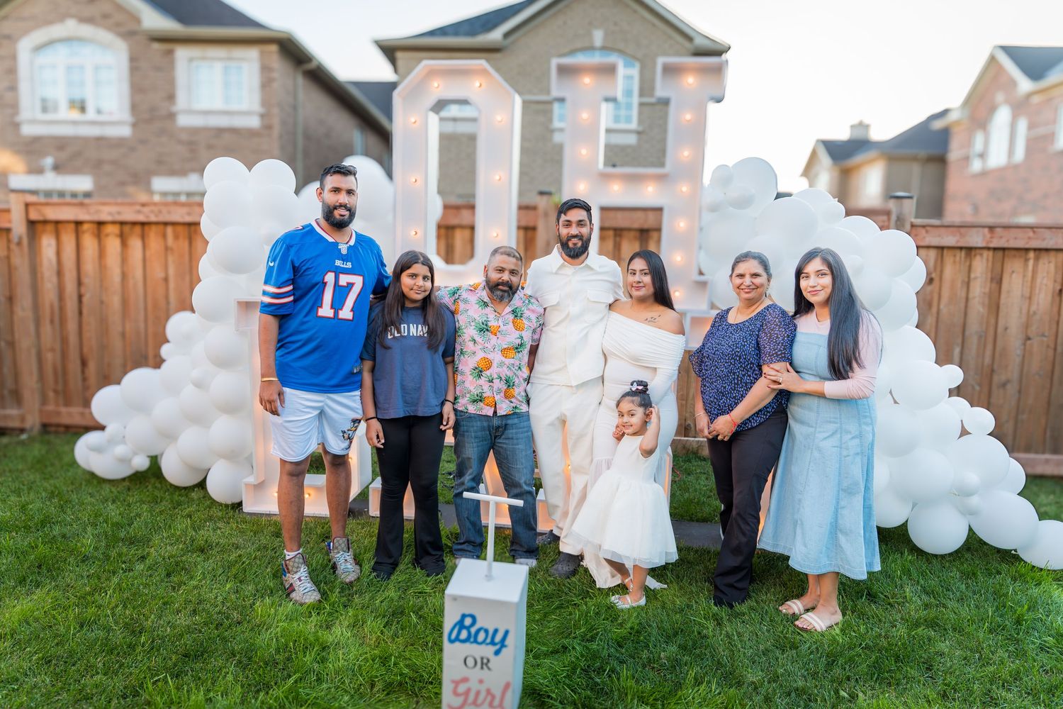 Family group photo at a gender reveal party with white balloon arch and Boy or Girl sign.