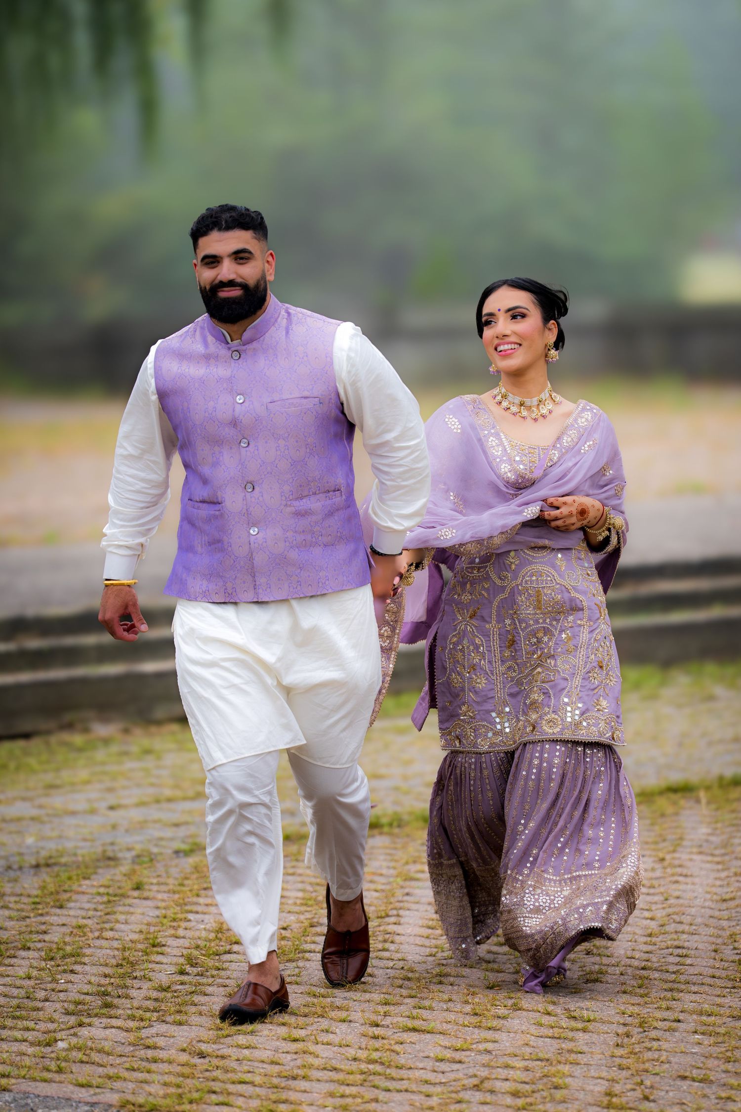 A couple runs playfully together wearing coordinated purple and white traditional outfits.