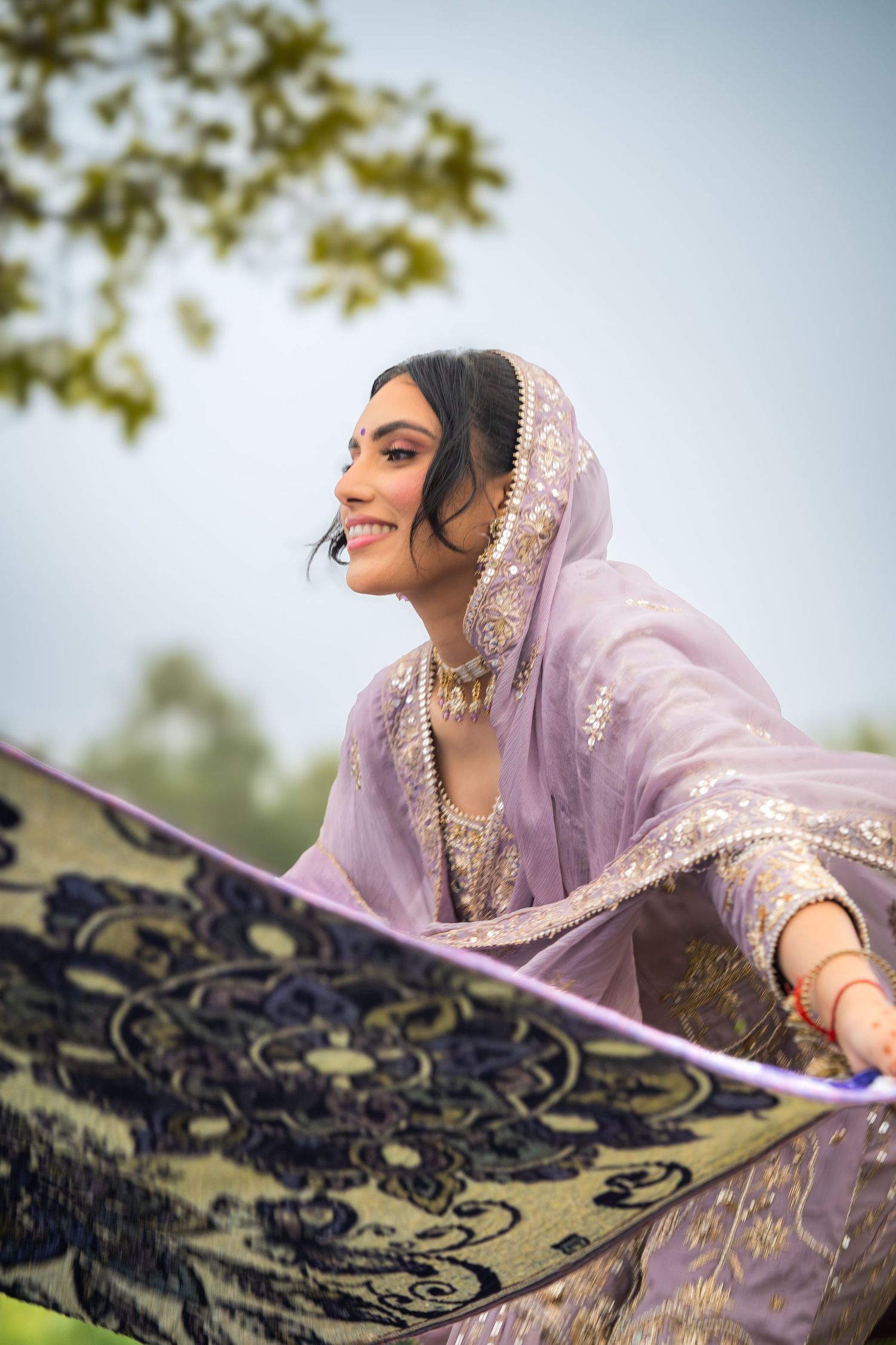 Ornate lavender outfit with gold details photographed with decorative blue textile in natural setting.