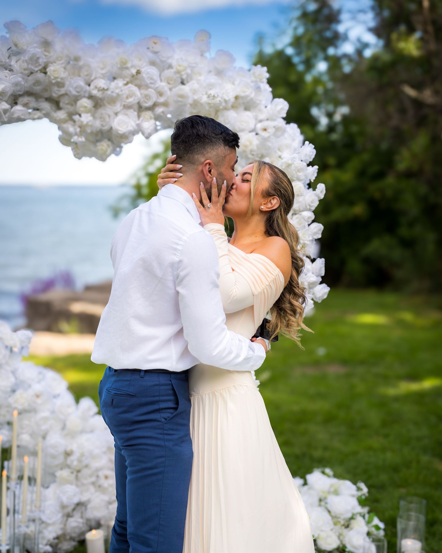 Romantic wedding ceremony under white floral arch in garden setting.