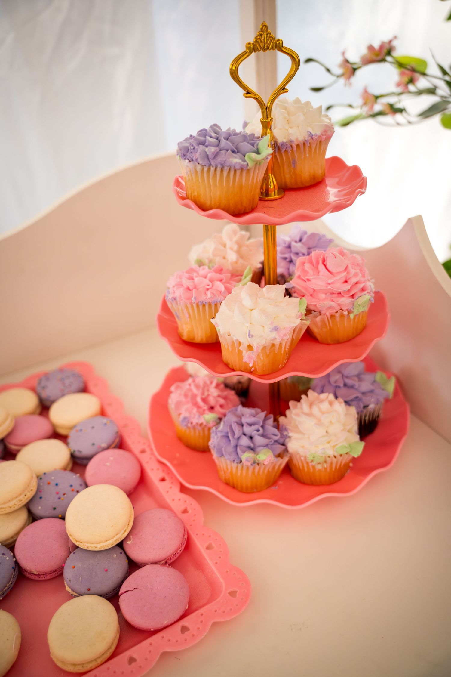 Three-tiered pink dessert stand displaying cupcakes with pink and purple frosting alongside macarons.