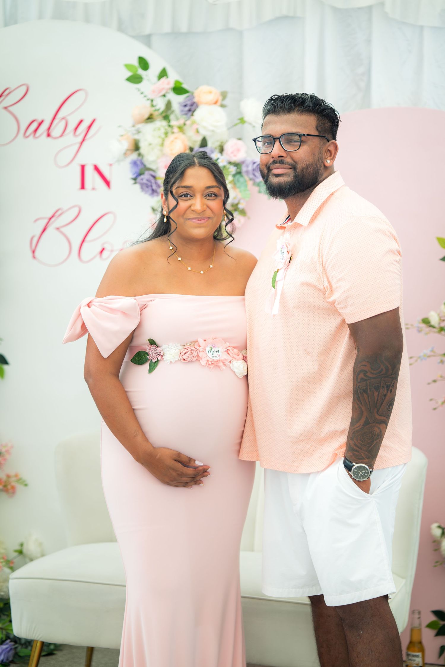 Happy couple poses at baby shower event with elegant floral decorations and matching pink attire.