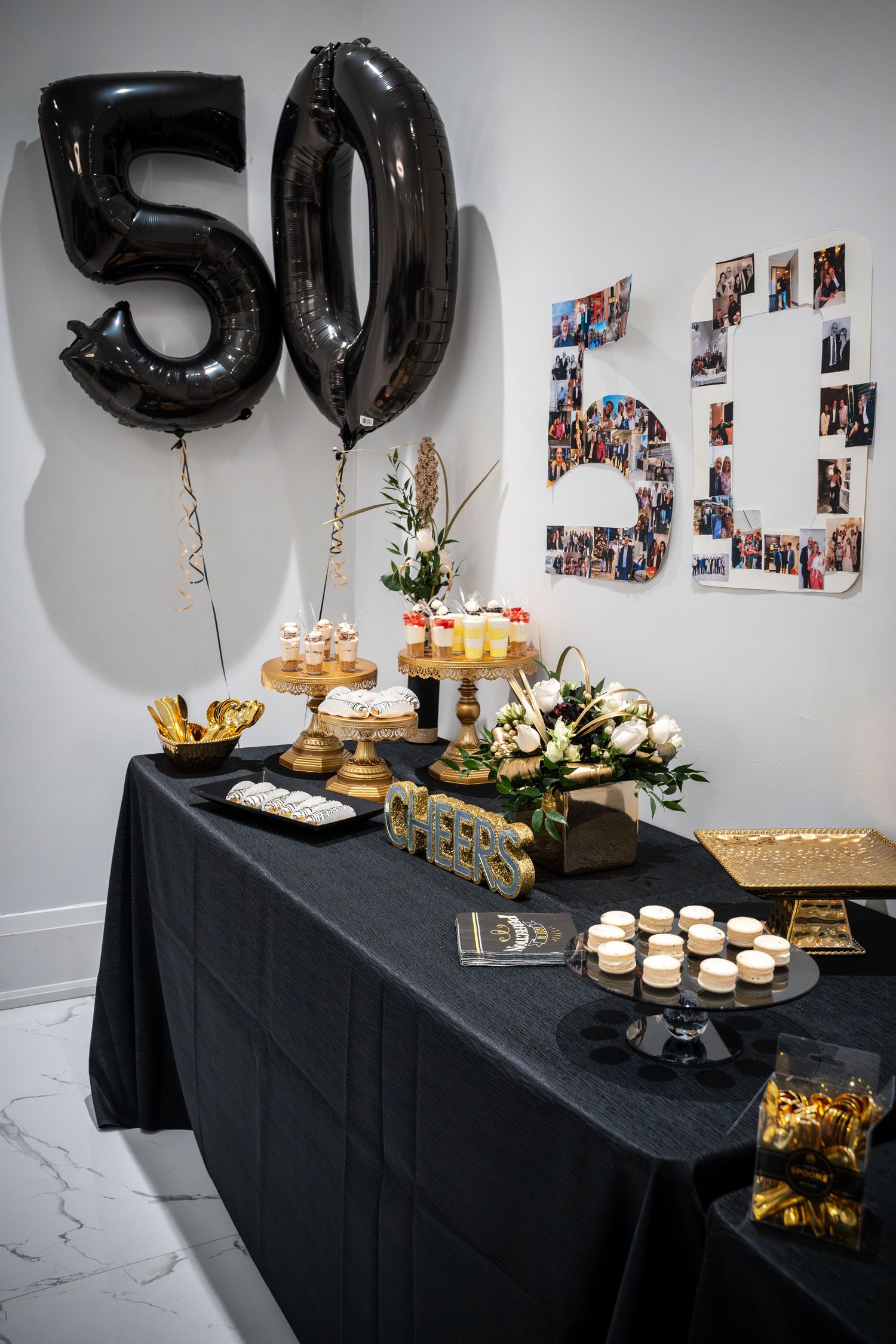 Party setup with black tablecloth, balloon numbers, and photo collage on wall.