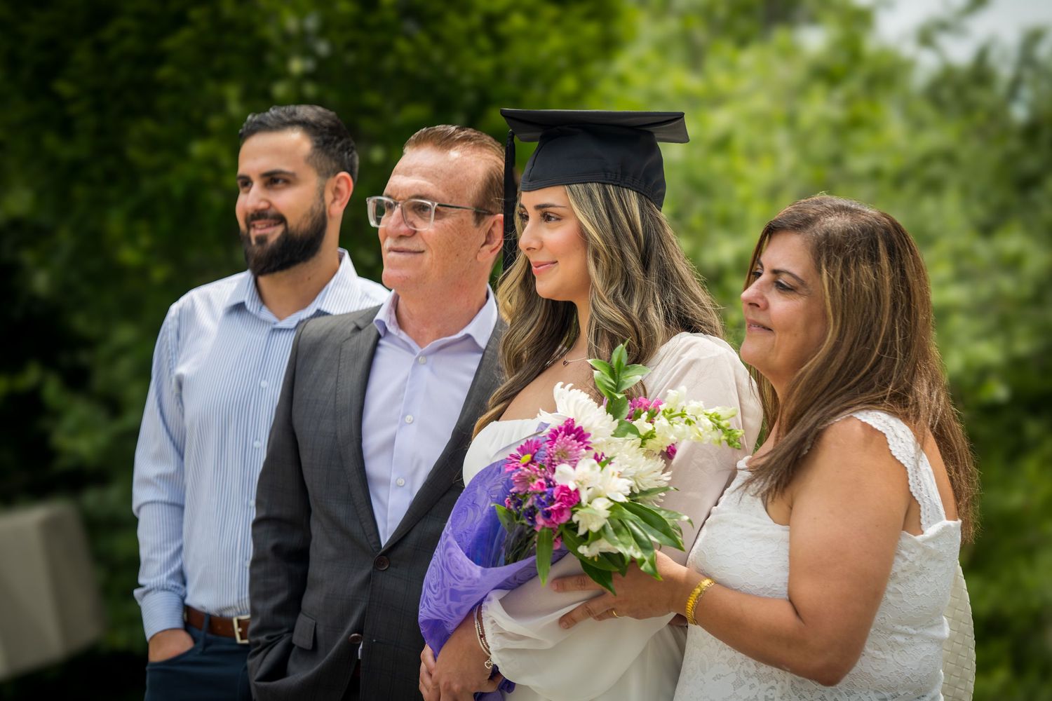 Wedding party poses outdoors in a garden setting with bright floral bouquets and formal attire.