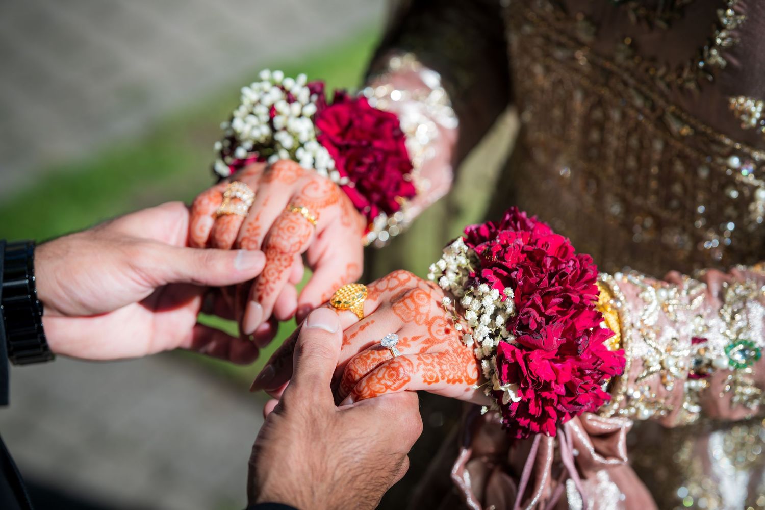 Close-up of hands with intricate henna designs holding red flowers during a wedding ceremony.