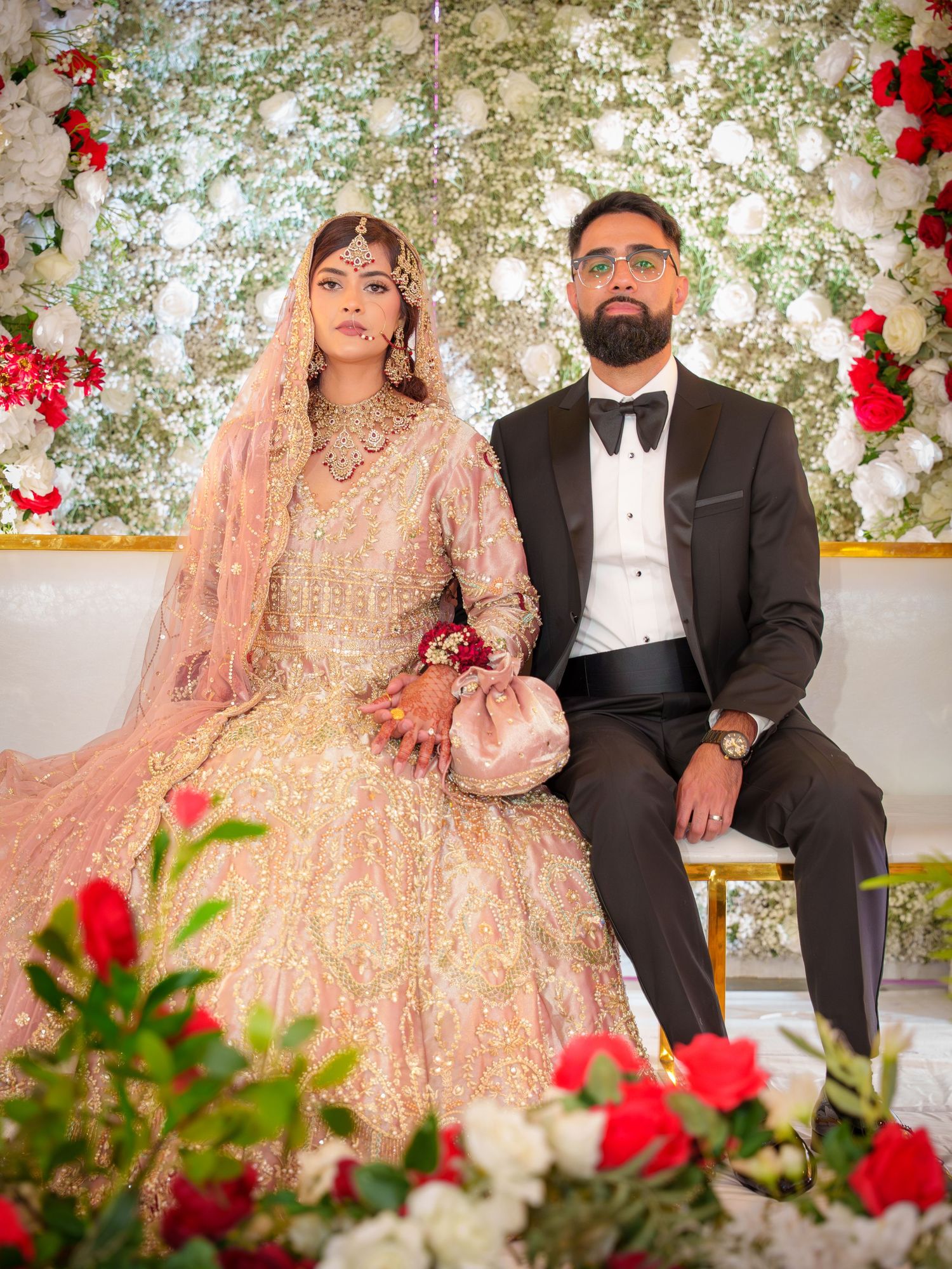 Wedding portraits against white floral wall with red roses and elegant decor.