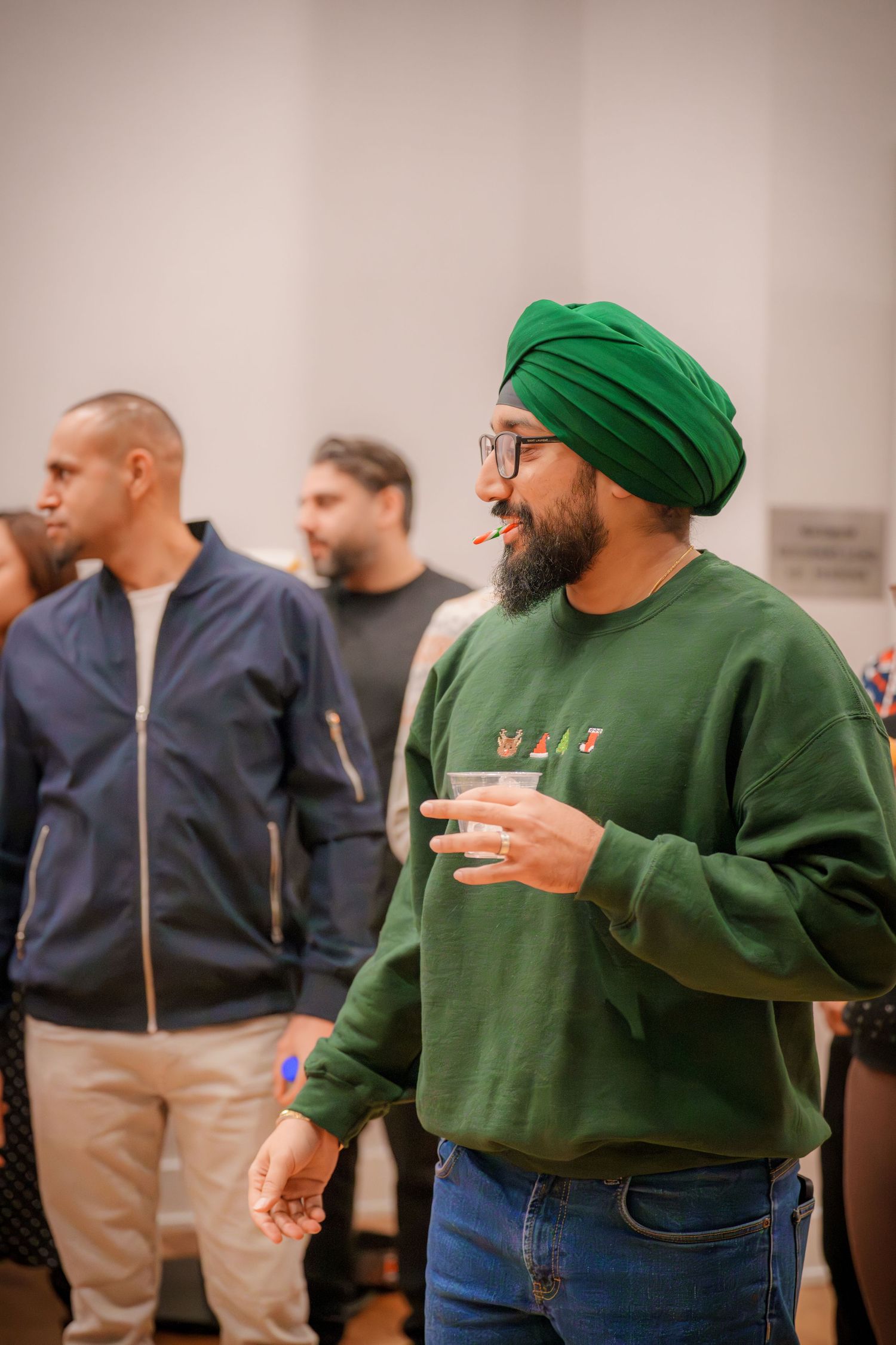 Person in a green sweater and beanie enjoying refreshments at an indoor gathering.