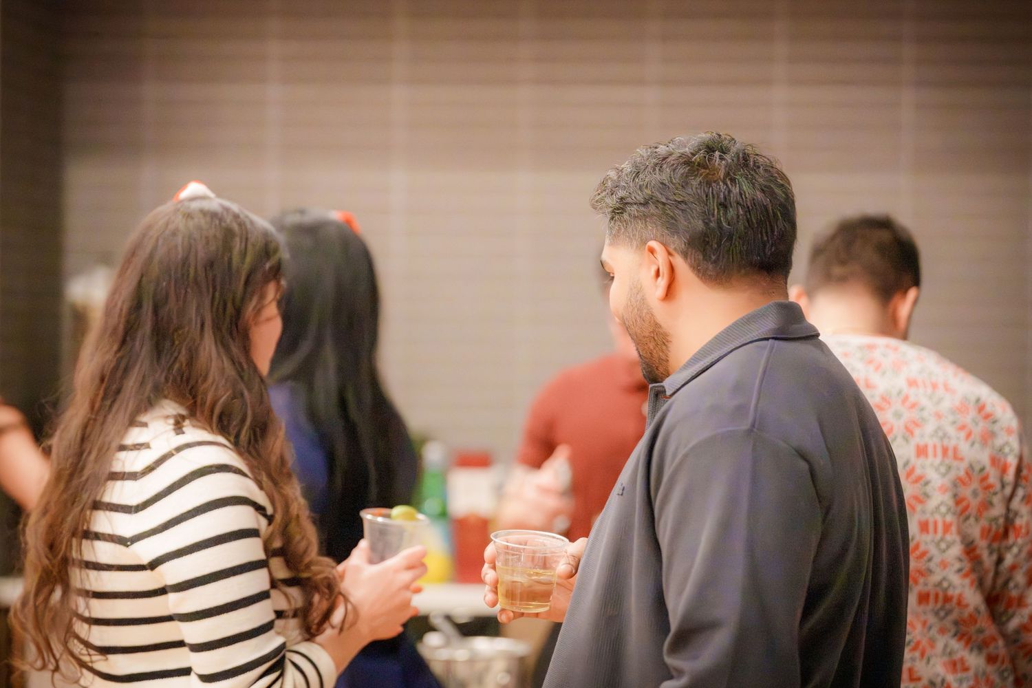 People mingling at a social gathering in an indoor space with dim lighting.
