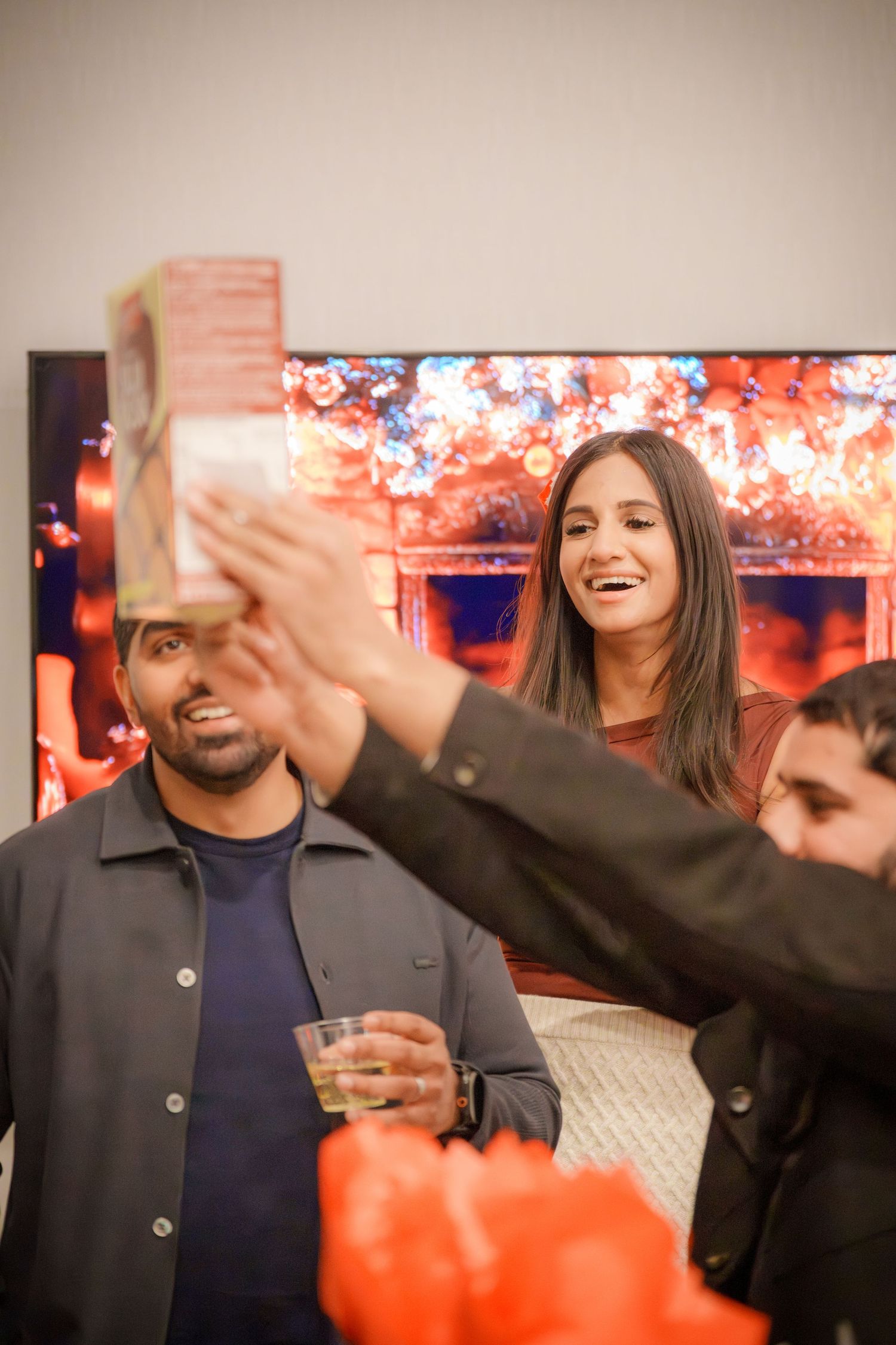People interact enthusiastically during a celebration with festive decorations visible in the background.
