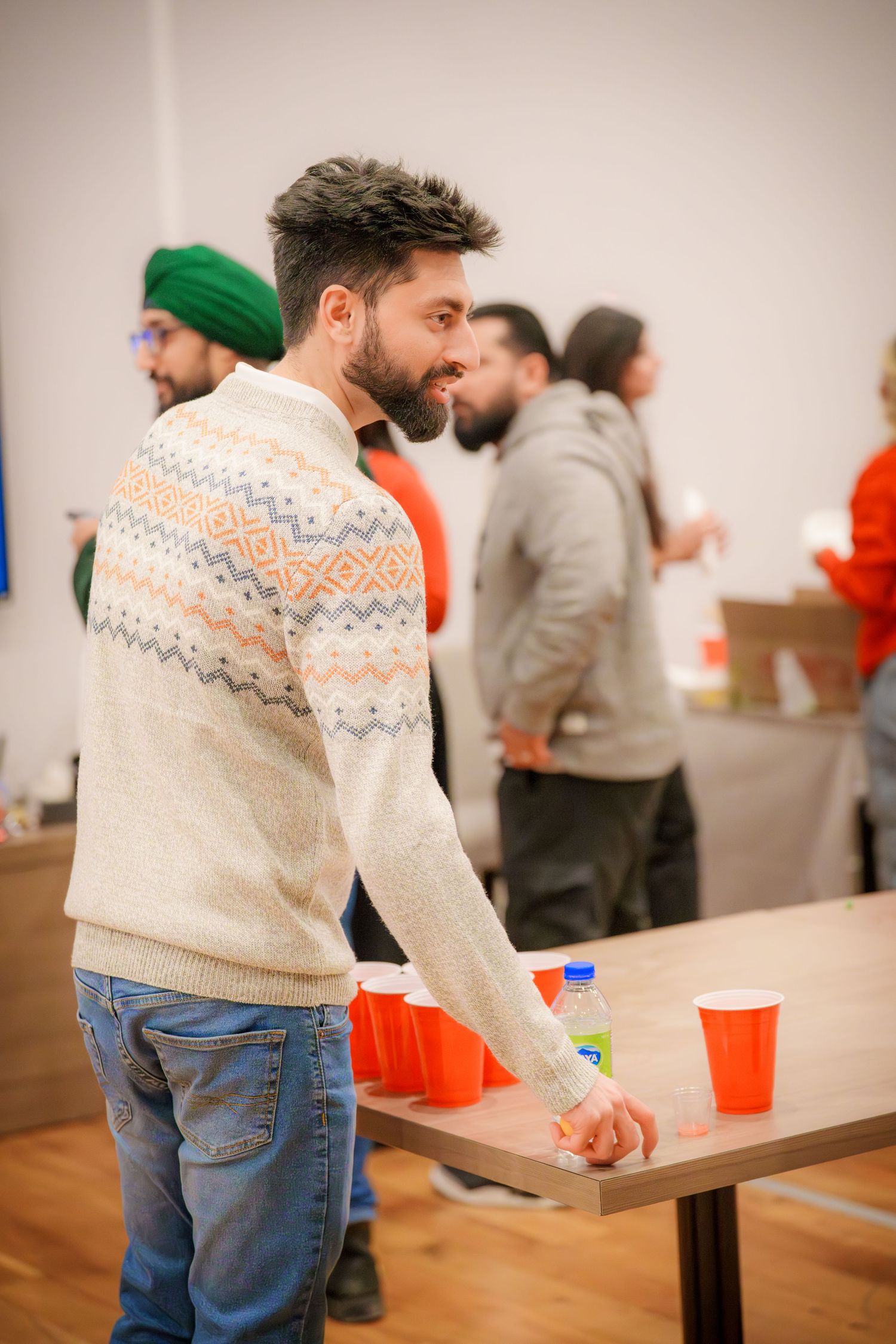 People playing beer pong at a party with red cups on long tables.