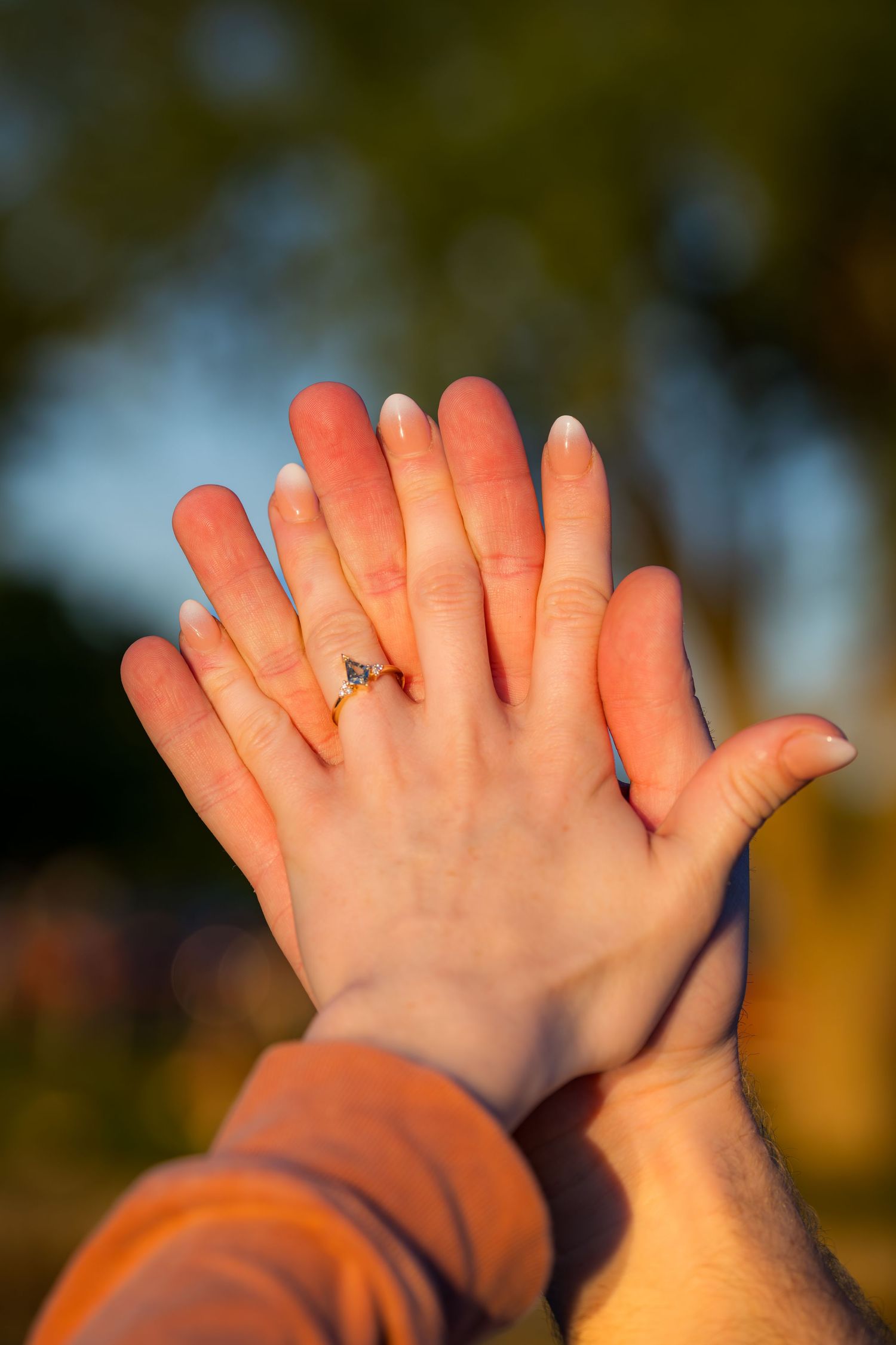 Two hands pressed together showing an engagement ring with diamond at golden hour outdoors.