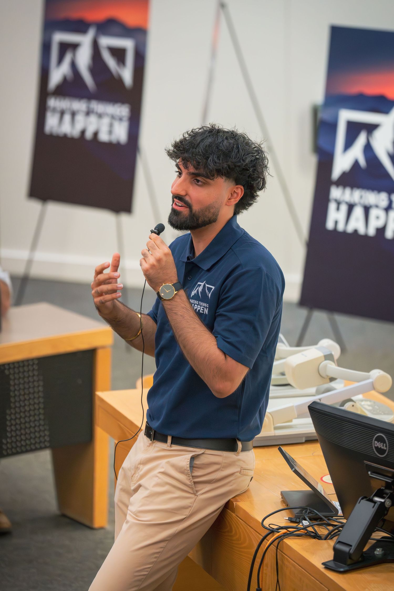 Person in blue shirt gesturing while speaking at a podium during a presentation.