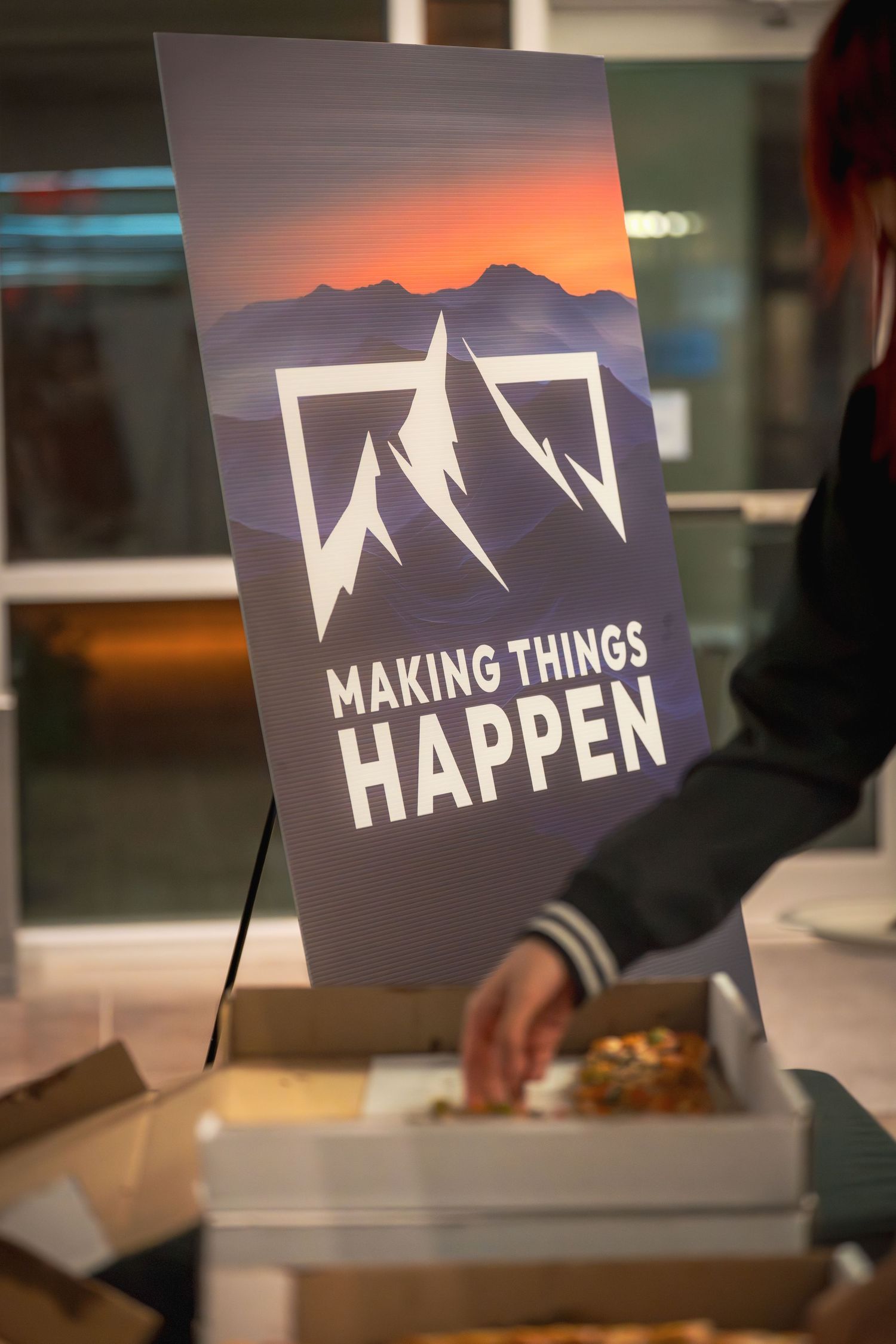 Display of 'Making Things Happen' logo signs with mountain design against dark background.