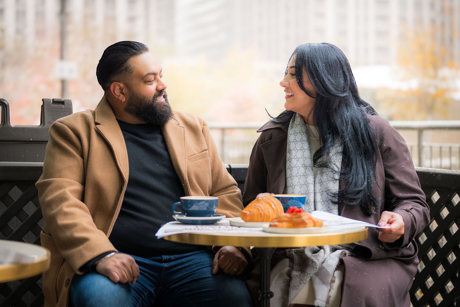 Couple enjoying coffee and conversation at an outdoor cafe table on a sunny afternoon.