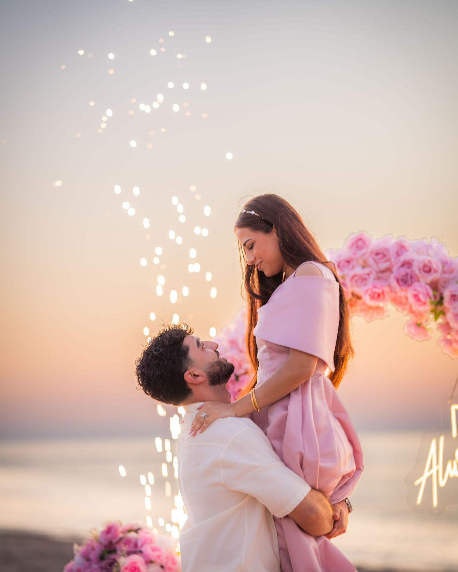 A romantic beach proposal with sparklers and pink floral decorations at sunset.