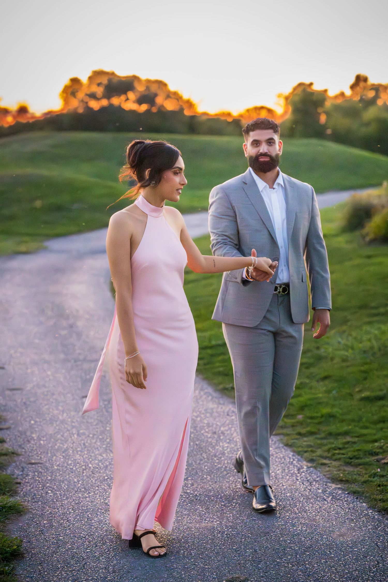 A couple takes a romantic evening walk on a gravel path surrounded by green grass.