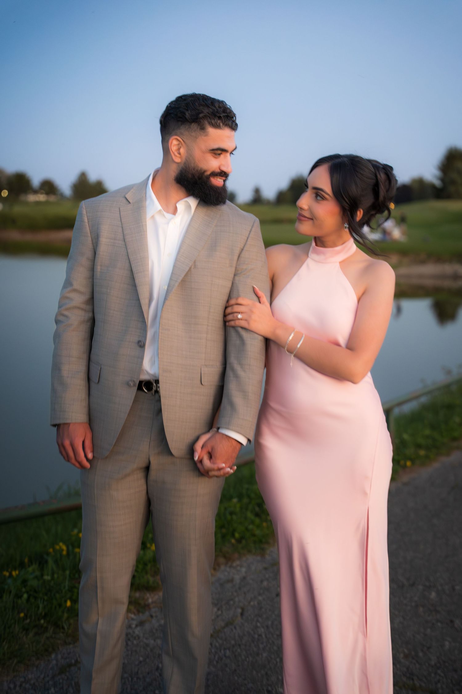 Couple in pink dress and grey suit poses together outdoors.