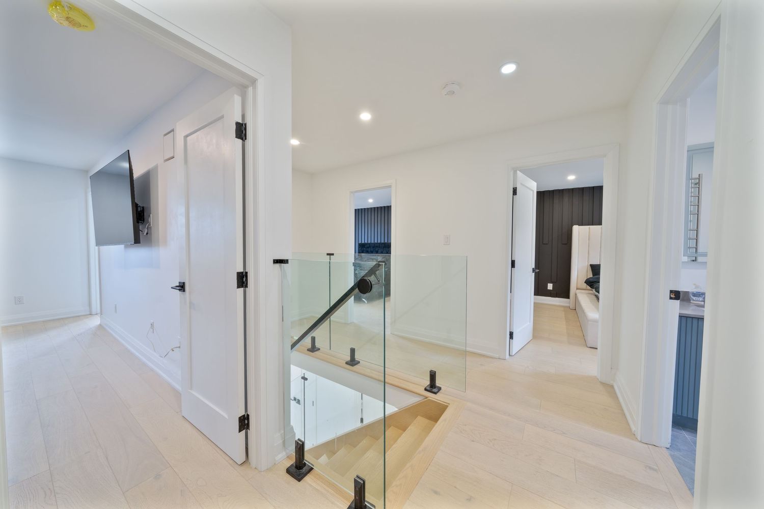 Modern white staircase with glass railings and pendant lights in a minimalist interior design.