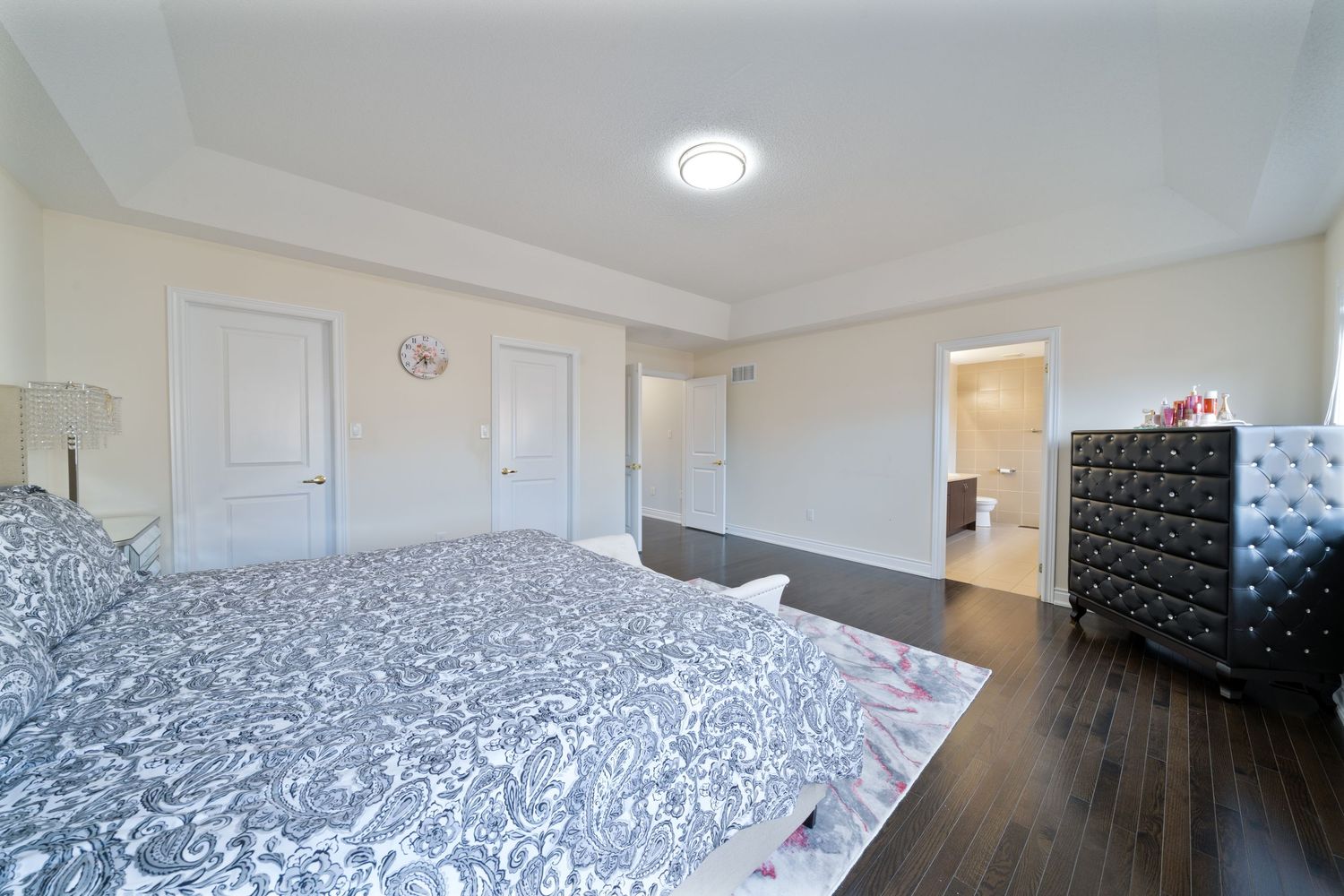 Modern bedroom with dark hardwood floors, black and white patterned bedding, and white doors against beige walls.