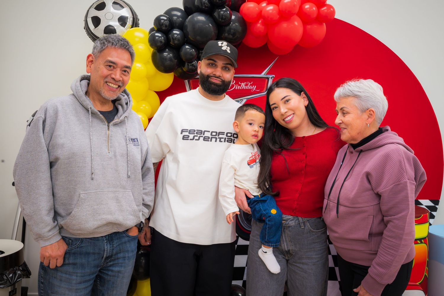 Family group photo at a festive Cars-themed birthday party with colorful balloons and decorations.