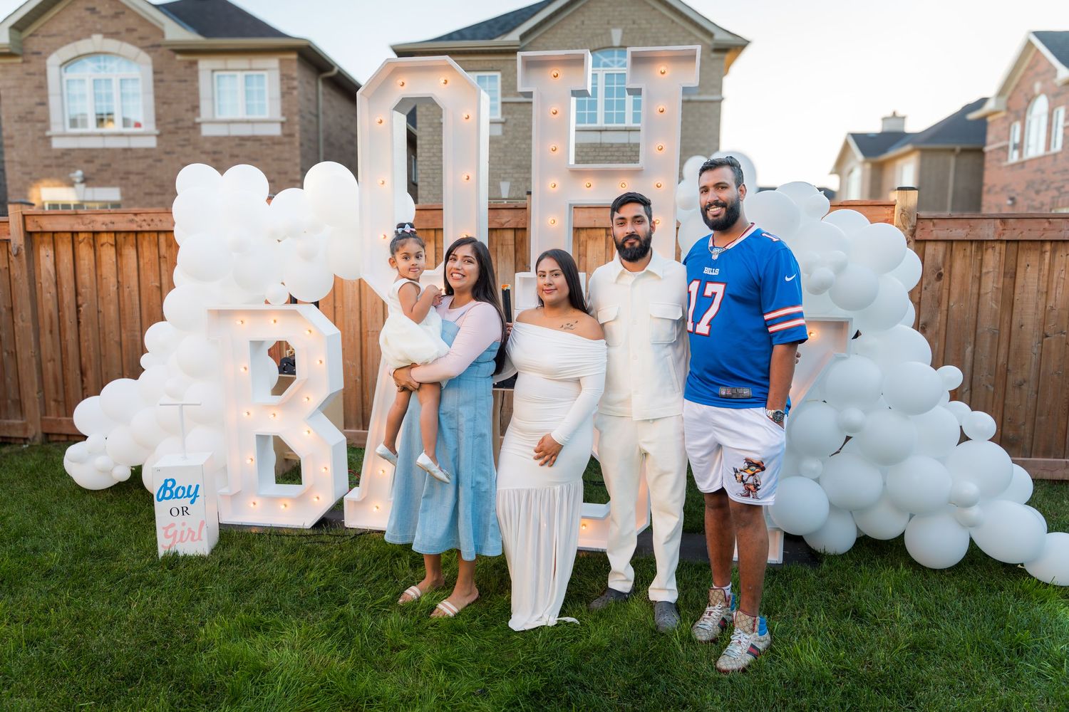 Family group poses in front of OH BABY marquee letters with blue and white balloon arch at gender reveal.
