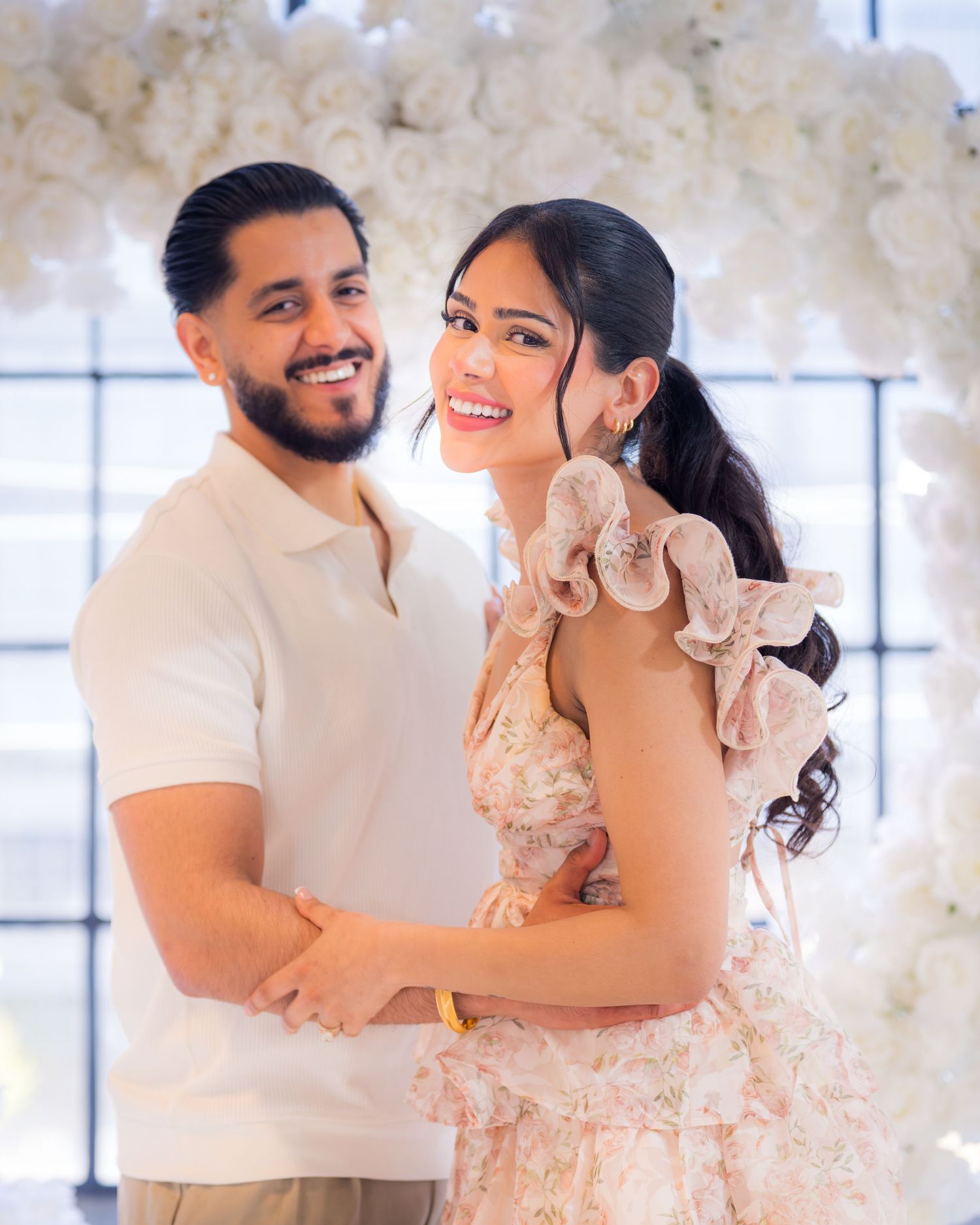 Happy couple embracing and smiling in front of a stunning white floral heart backdrop.