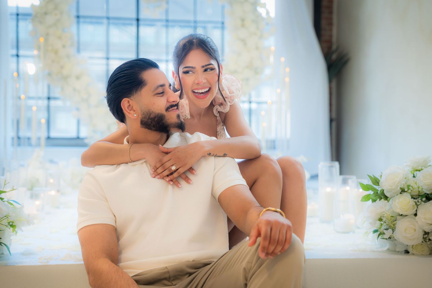 A smiling couple embraces lovingly in an elegant white floral decorated venue.