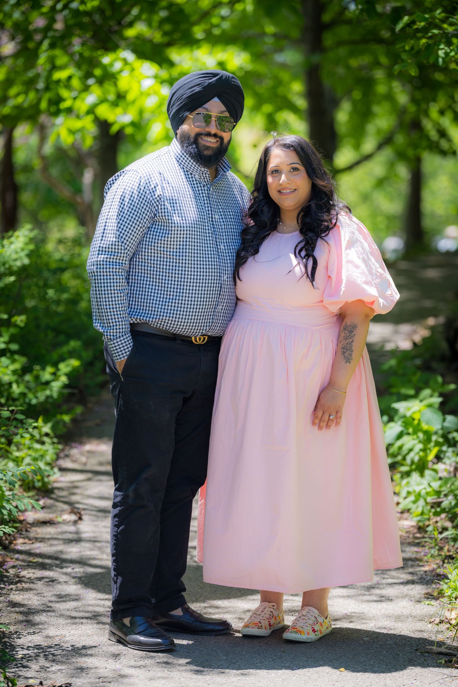 Couple posing on garden path, man in black turban and plaid shirt with woman in pink dress.