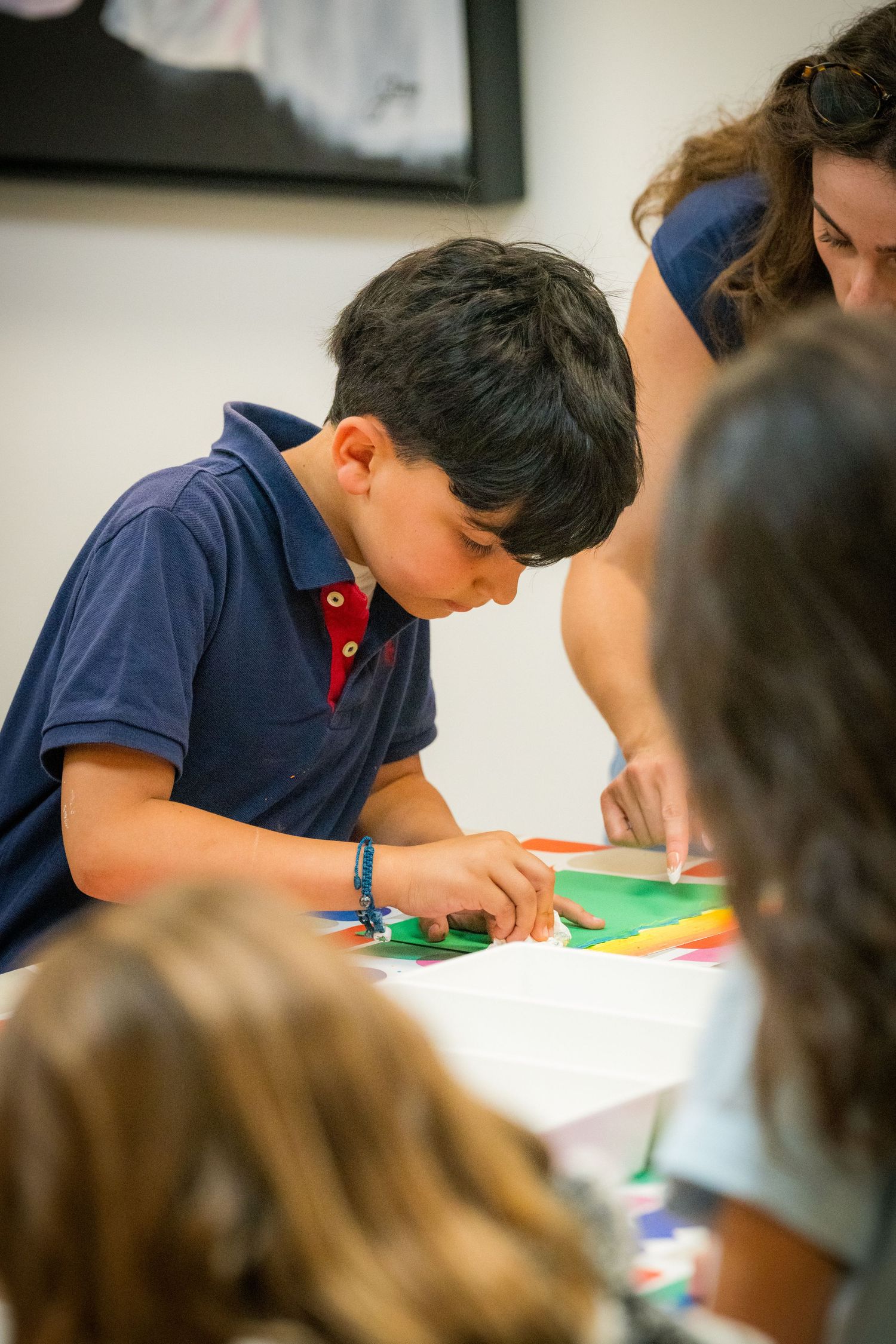 A focused young boy works on a colorful paper collage art project with an instructor nearby.