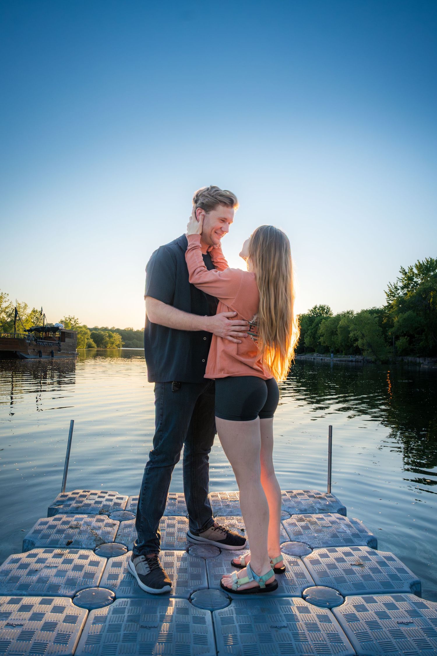 Happy couple embracing on a floating dock by a serene lake during a golden sunset.
