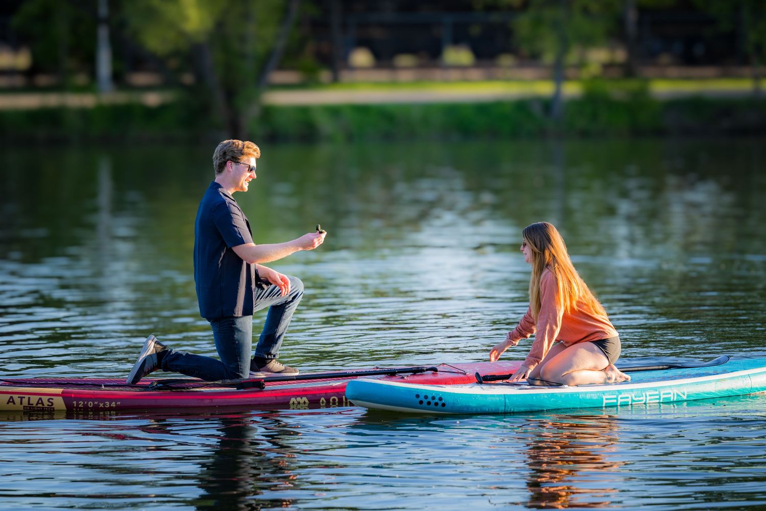 Romantic marriage proposal on paddleboards on a peaceful lake at sunset.