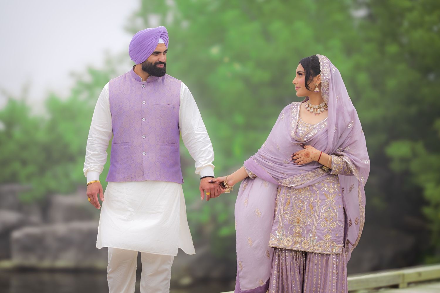 A couple in traditional Punjabi dress walks together on a garden path during their photoshoot.