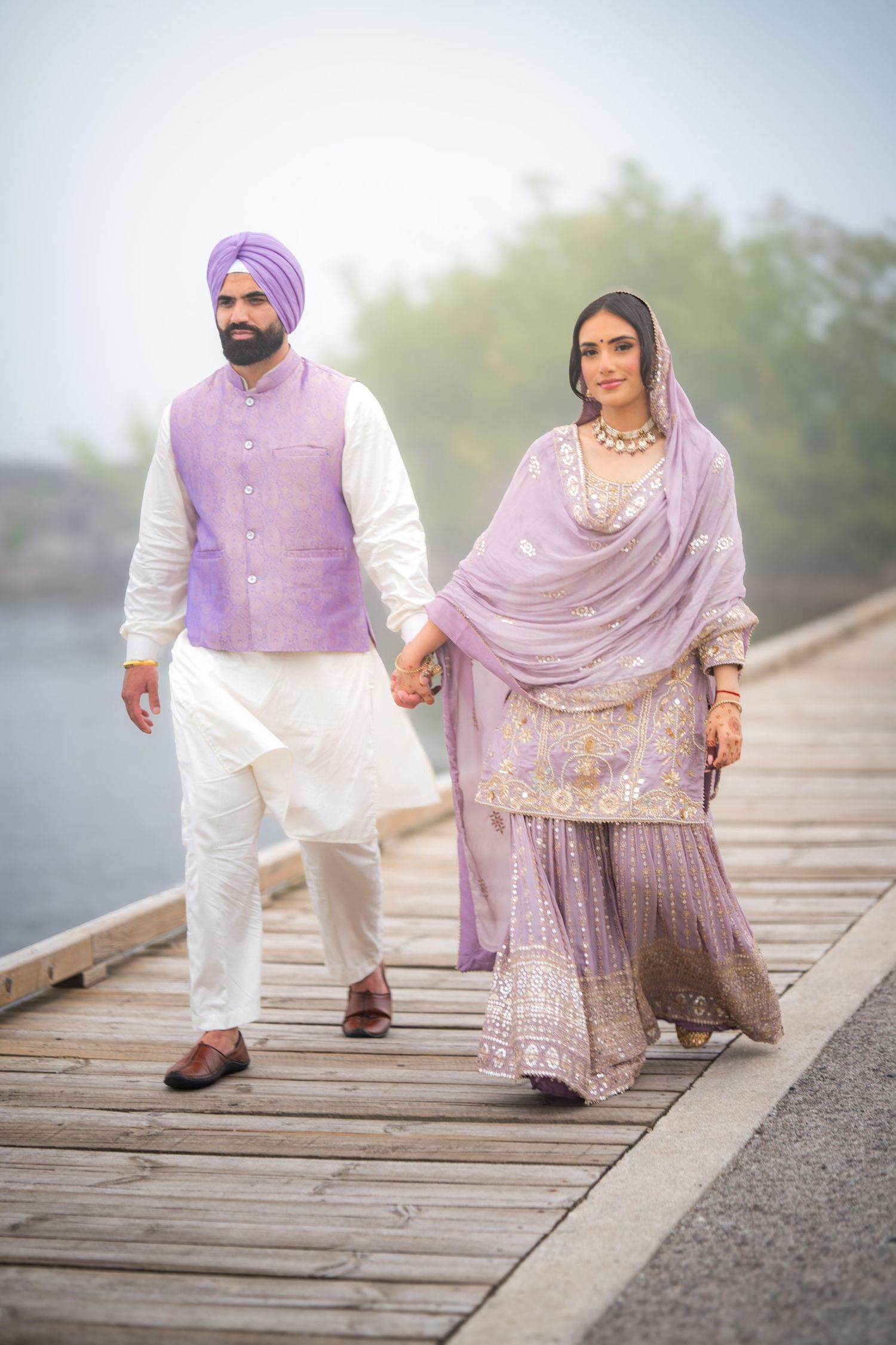 Couple in purple and white traditional dress walking together on a wooden boardwalk.