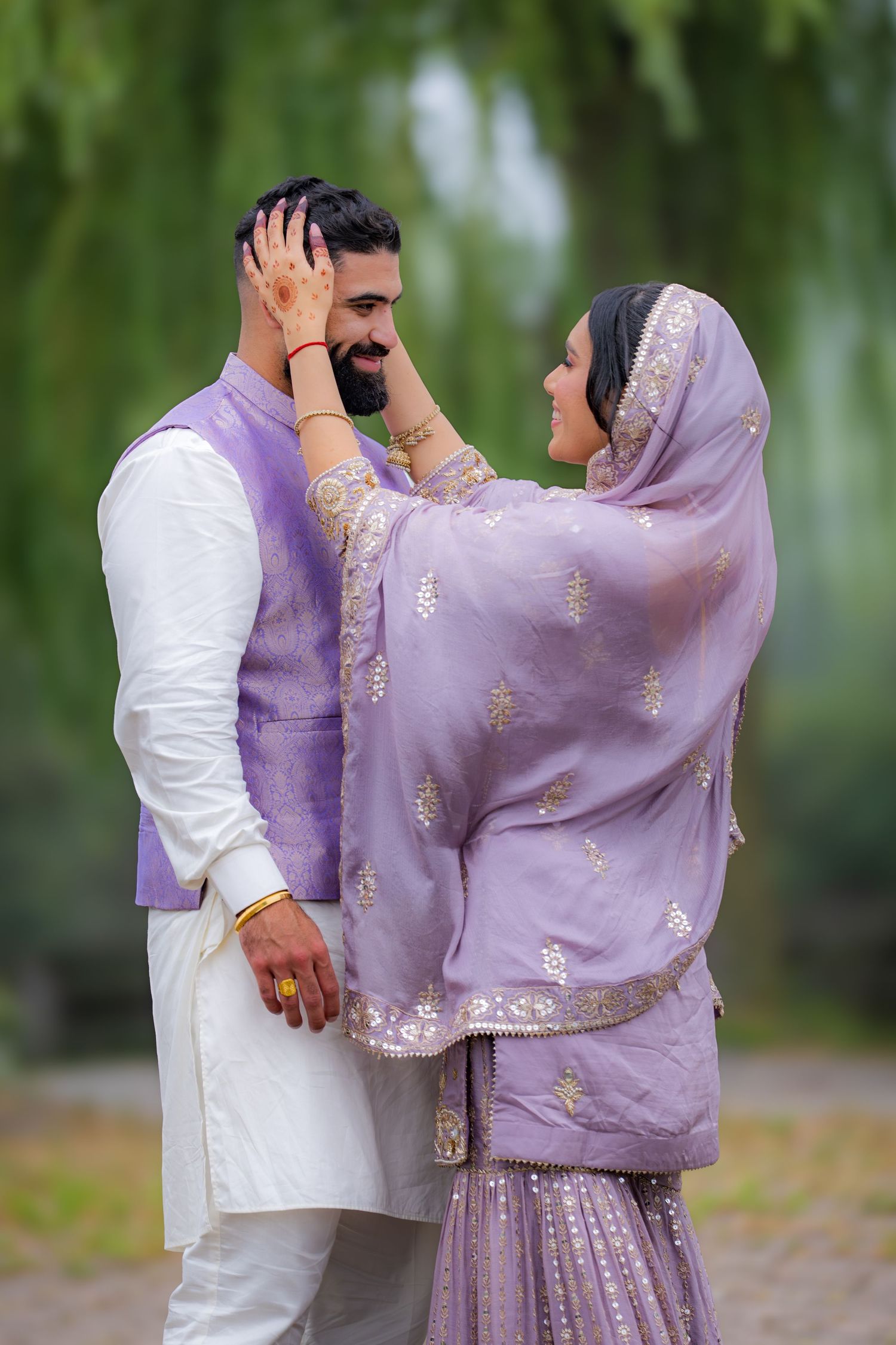 A couple in coordinated purple and white traditional outfits shares an intimate moment outdoors.