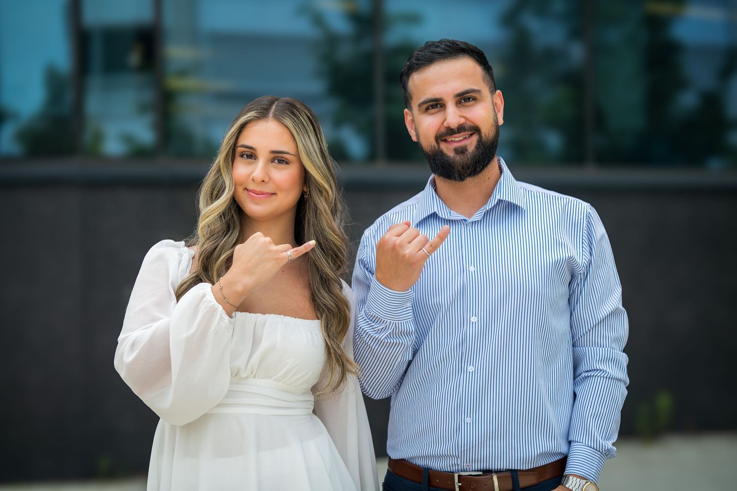 A couple stands close together smiling in front of a modern building exterior.