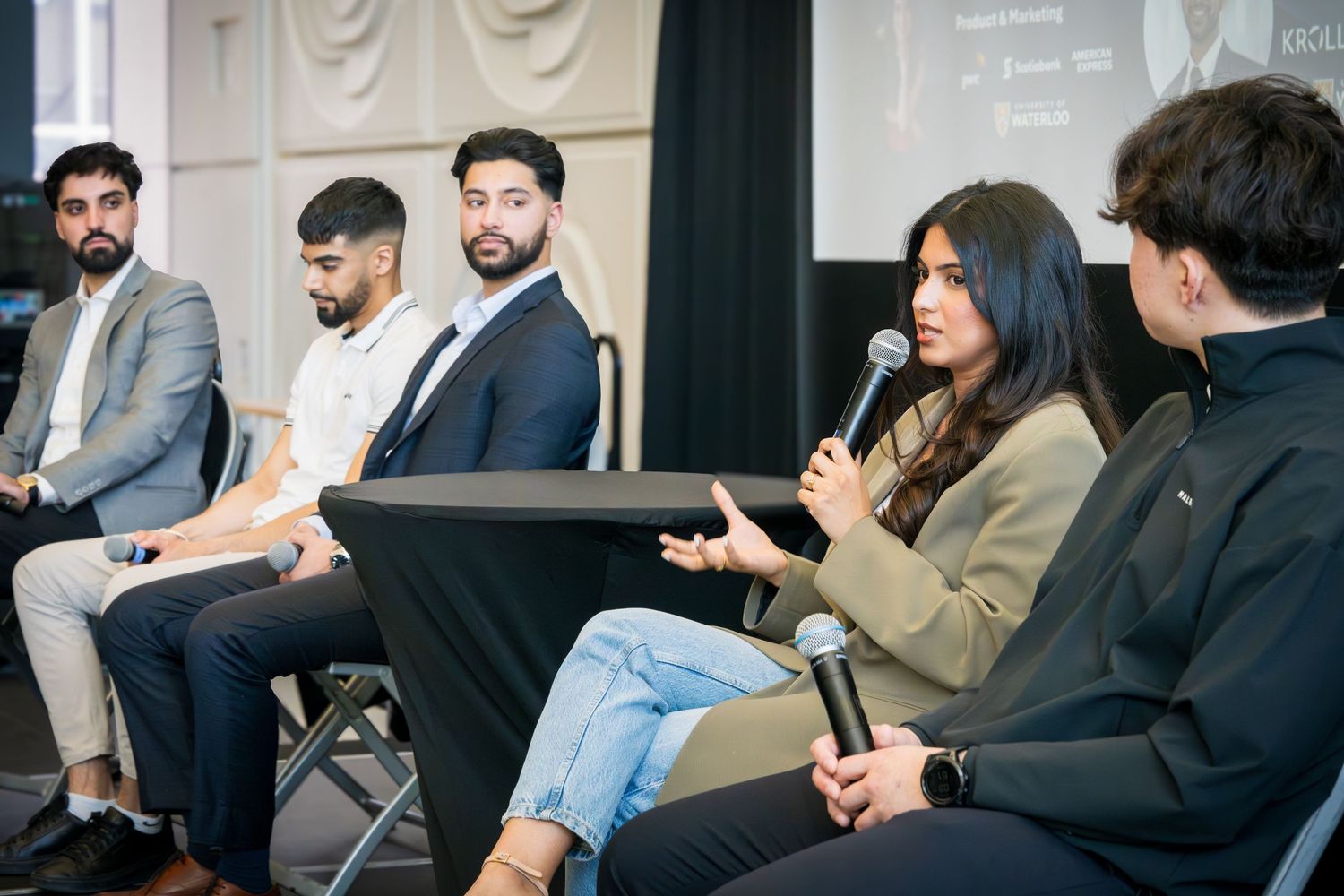 Business panel discussion with speakers seated in a row on stage during a professional event.