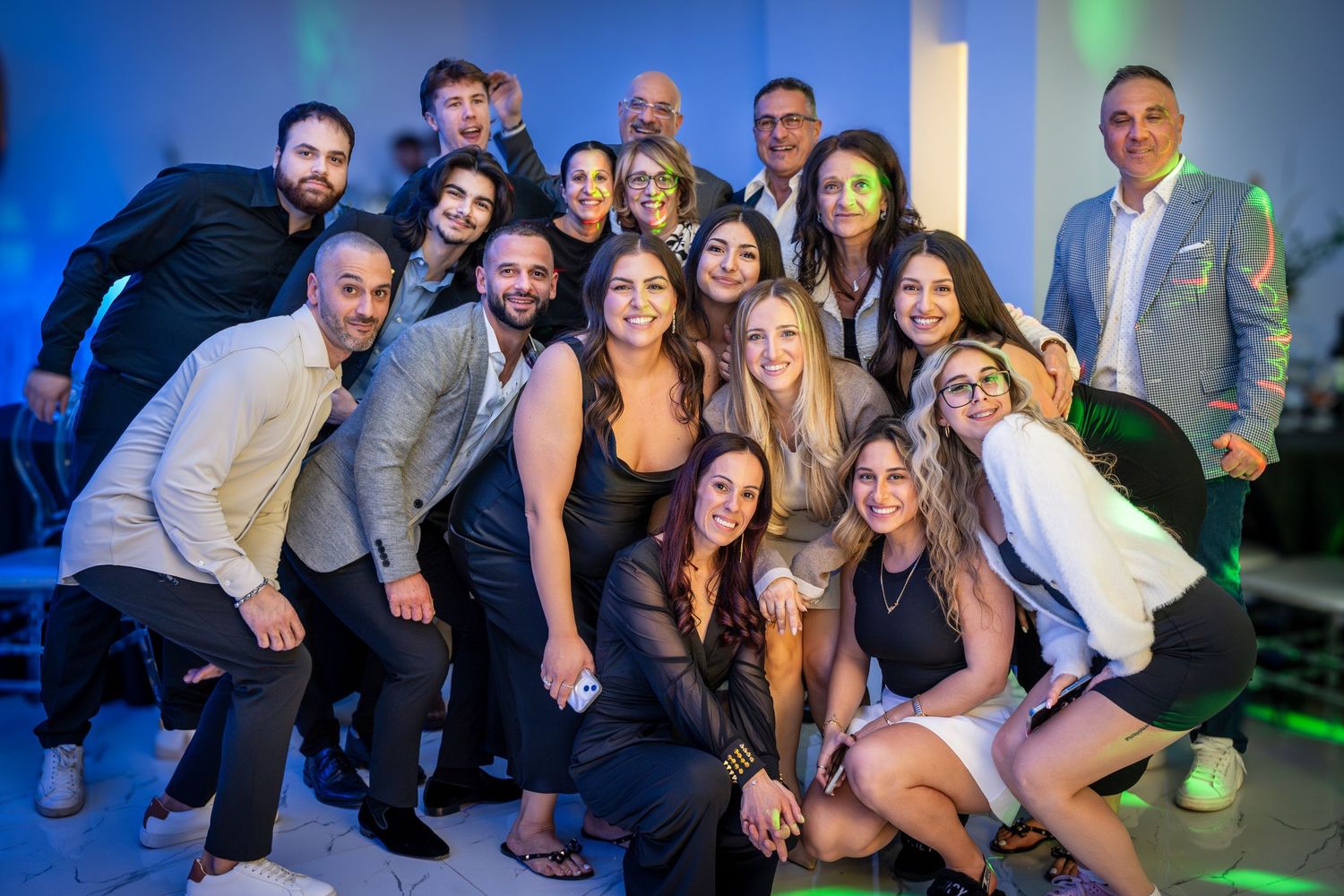 Large group photo of party attendees posing together under colored lighting.