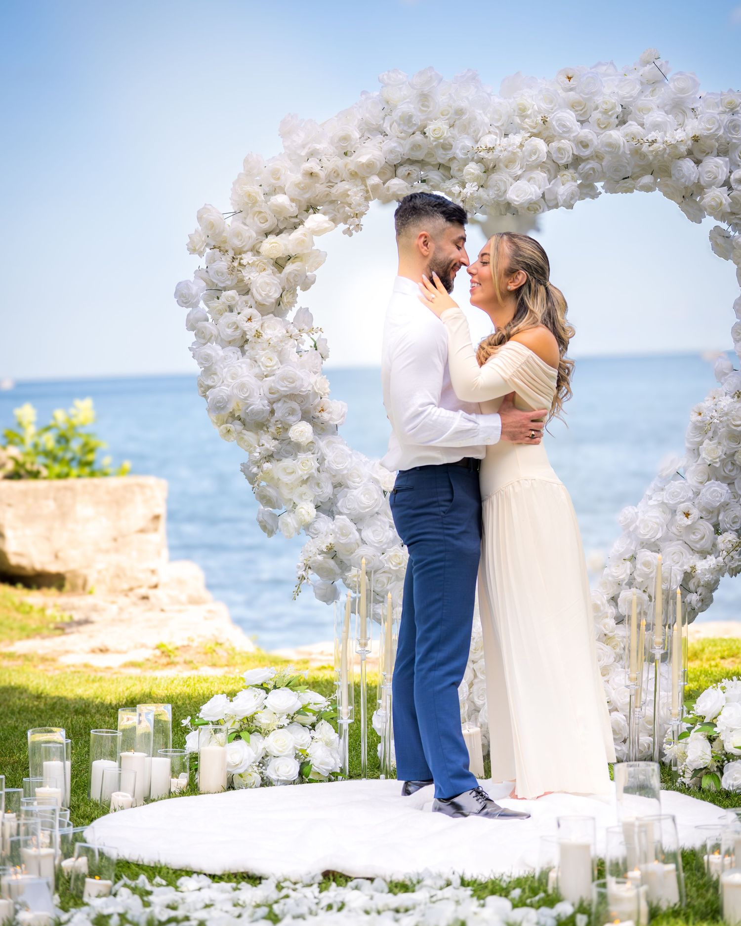 Romantic wedding ceremony by the ocean with white floral decorations and candlelit aisle.