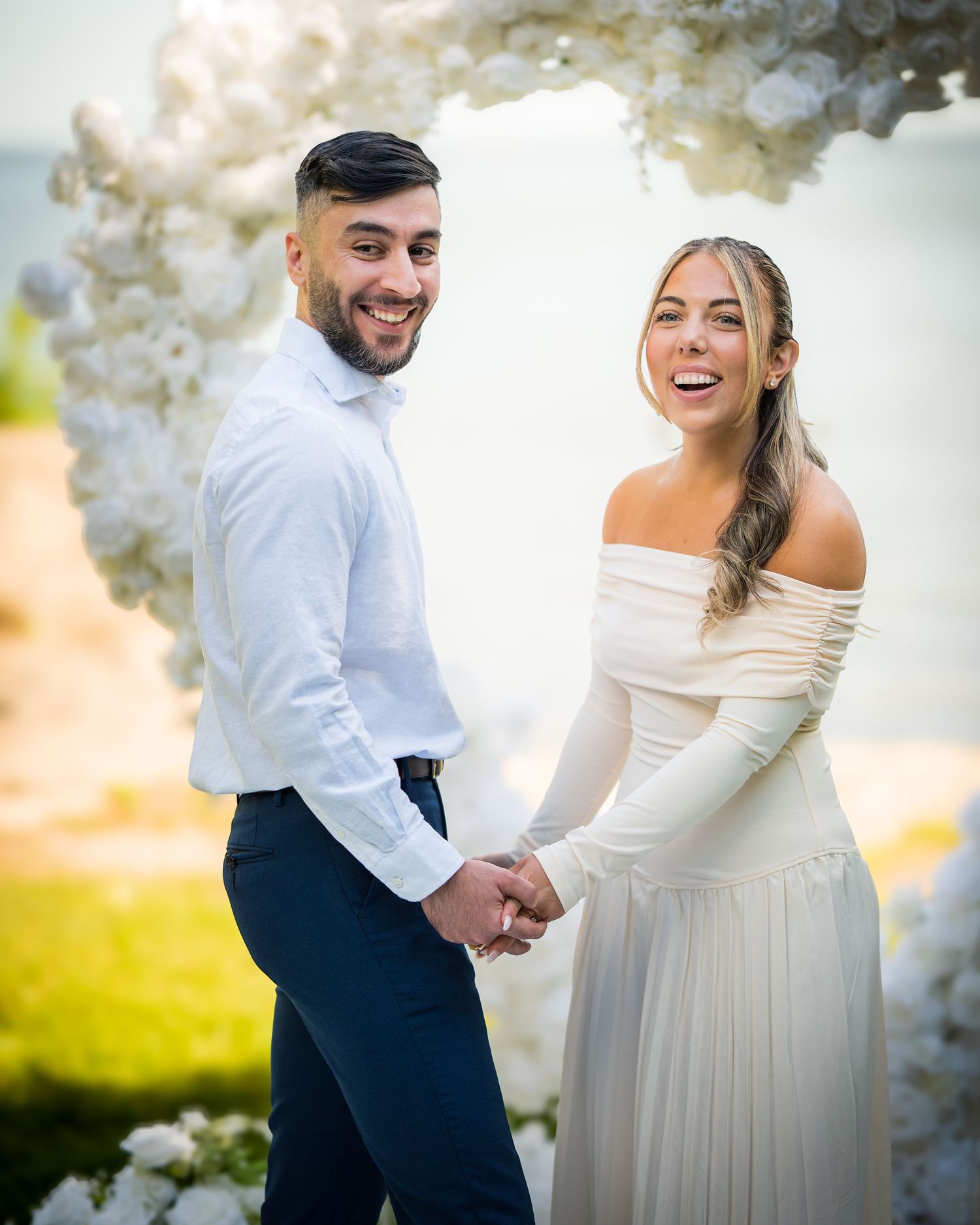 Couple sharing a joyful moment while dancing outdoors under white floral arrangements.
