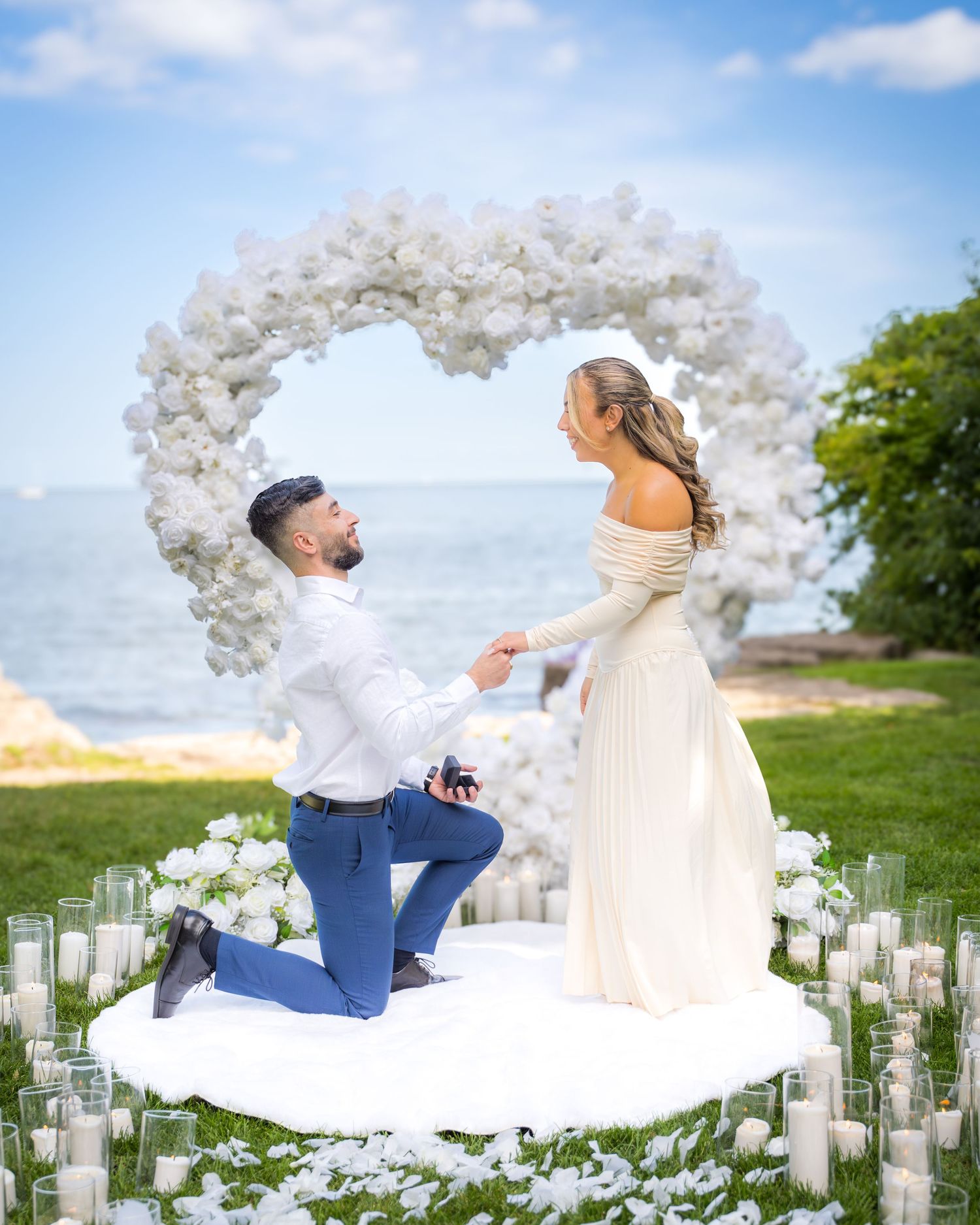 Seaside proposal setup with elegant white balloon arch and pathway lined with candles.